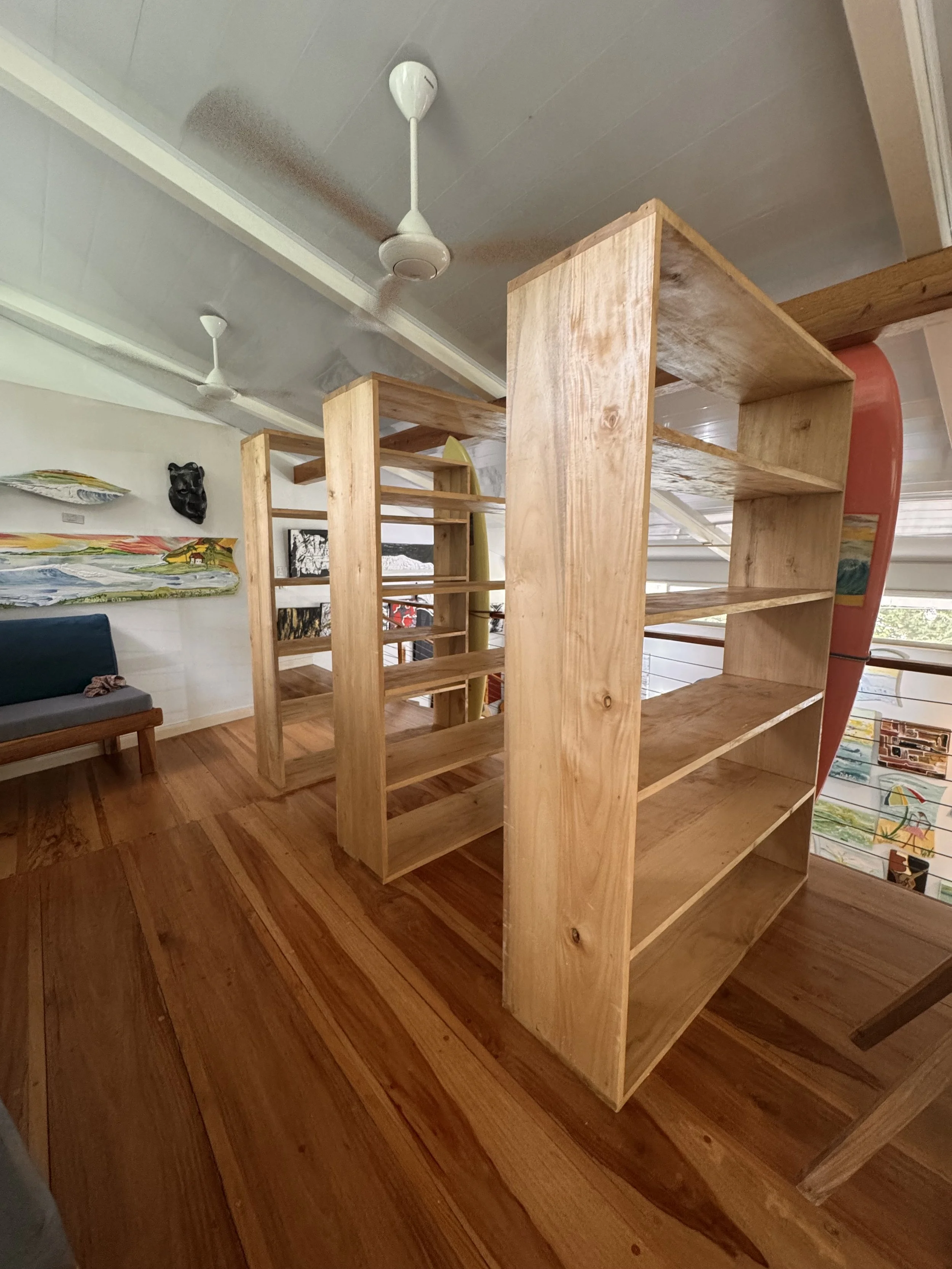 Unfinished wooden shelves and a corner of a room with art on the wall, a ceiling fan, and a window.