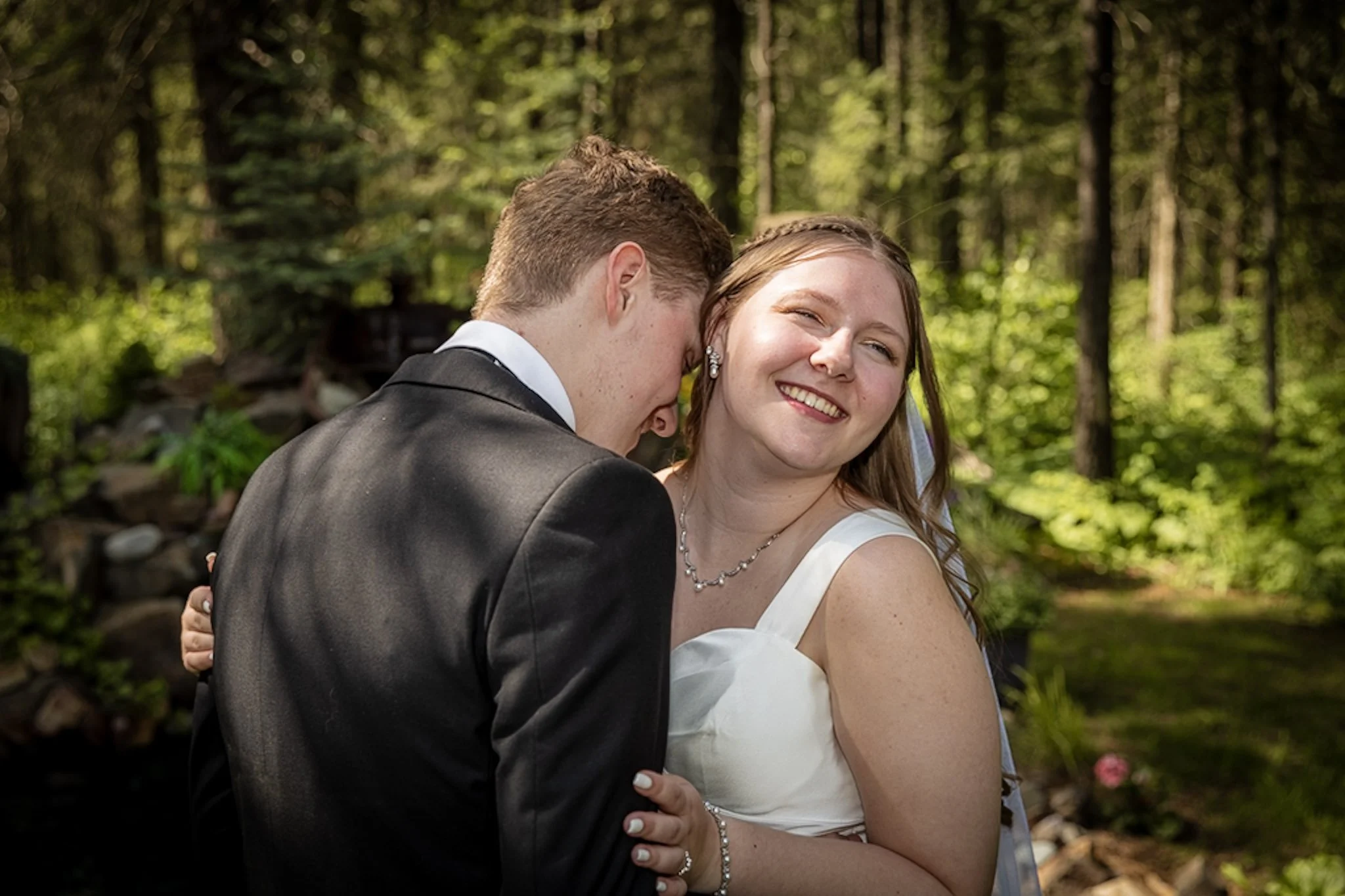 A couple sharing an intimate dance outdoors, surrounded by lush green trees and natural light.