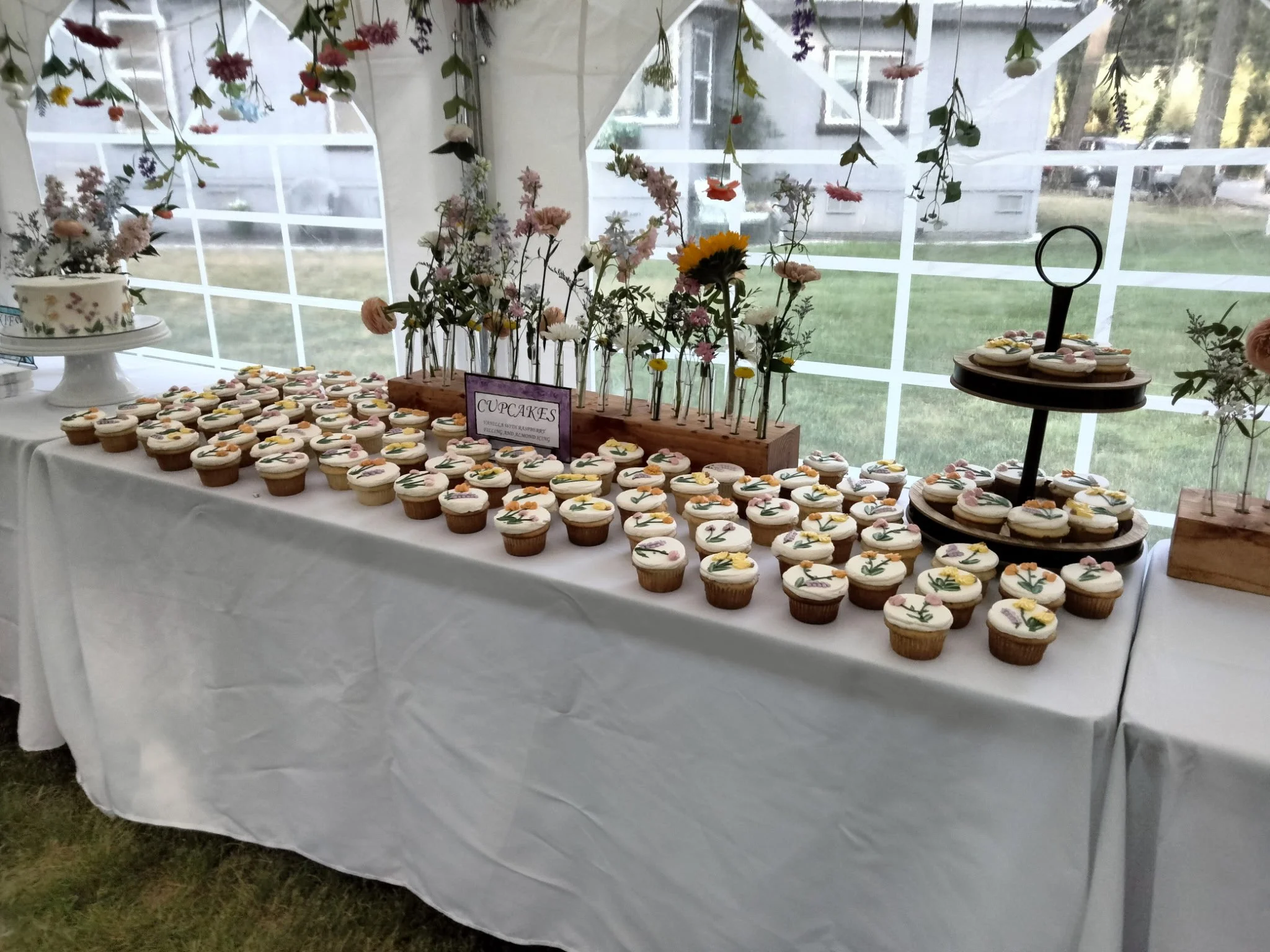 Table with decorated cupcakes and flower arrangements in a tent for a celebration.