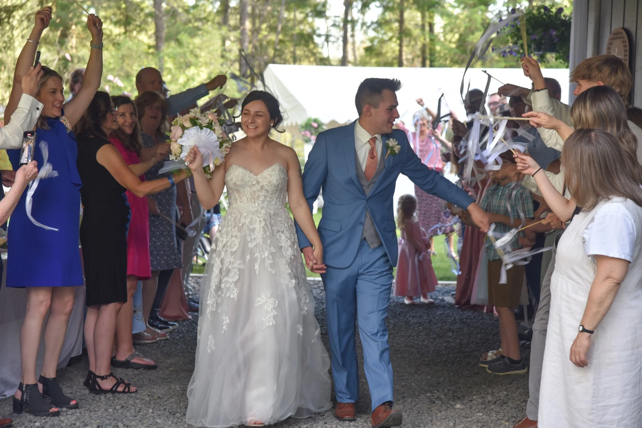 A newlywed couple walking hand-in-hand through a tunnel of guests at a wedding celebration, with guests holding sparklers and cheering.