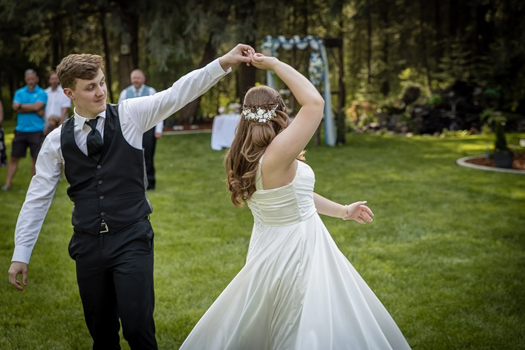 A wedding couple dancing outdoors with guests watching in the background.