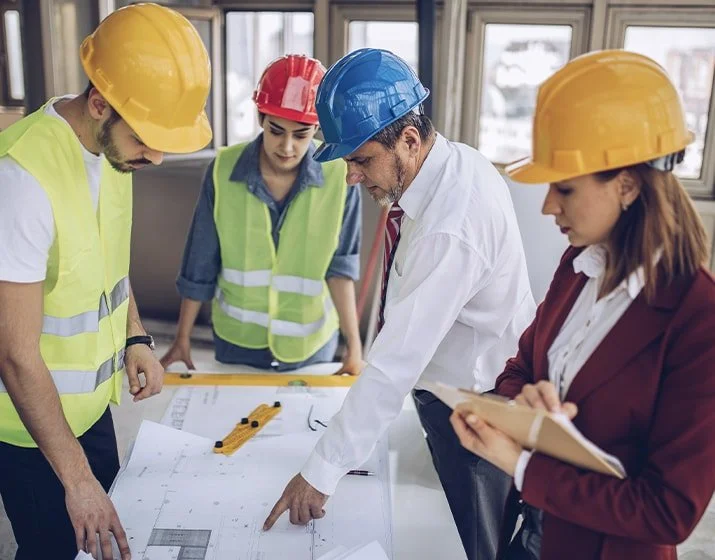 Four facility managers reviewing architectural drawings at a job site.