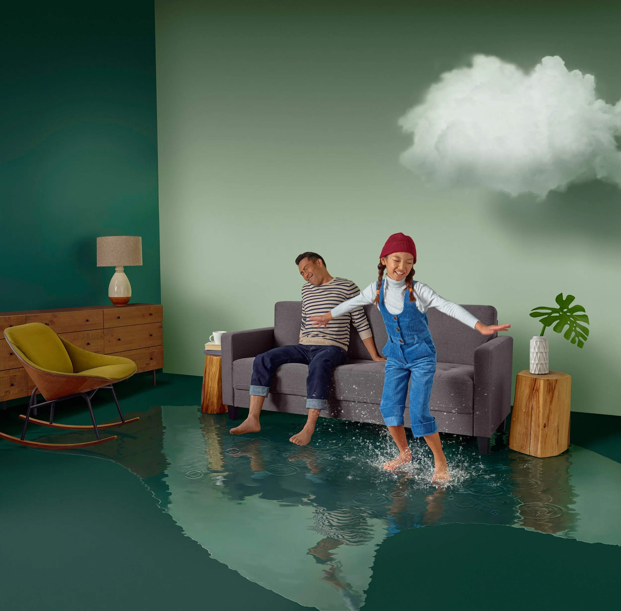 A man and a girl playing with water on the floor of a living room with a painted wall, furniture, and indoor plants.