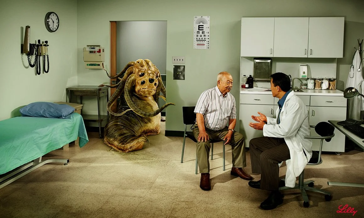 A doctor talking to an elderly patient in a hospital examination room with a large, fictional creature resembling a mix between a dog and a creature with multiple horns in the background.
