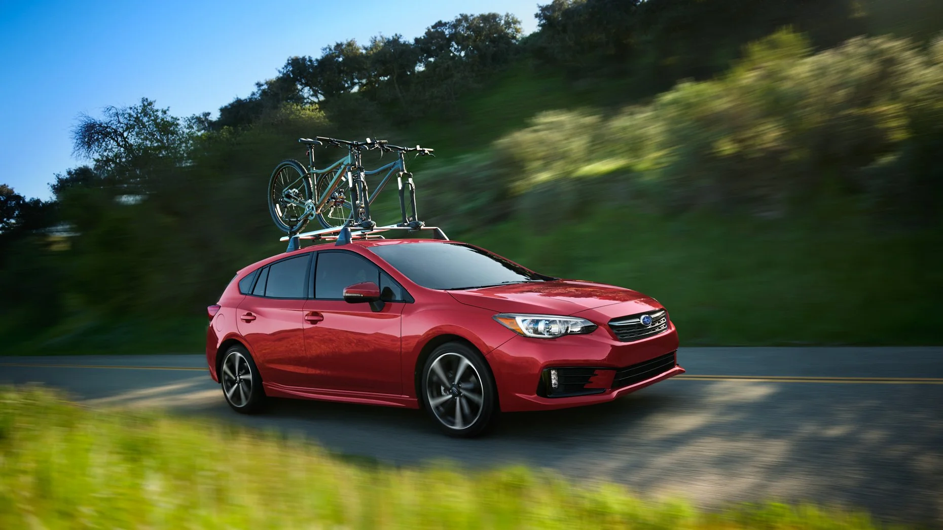 Red Subaru car driving on a paved road with a bicycle mounted on the roof.