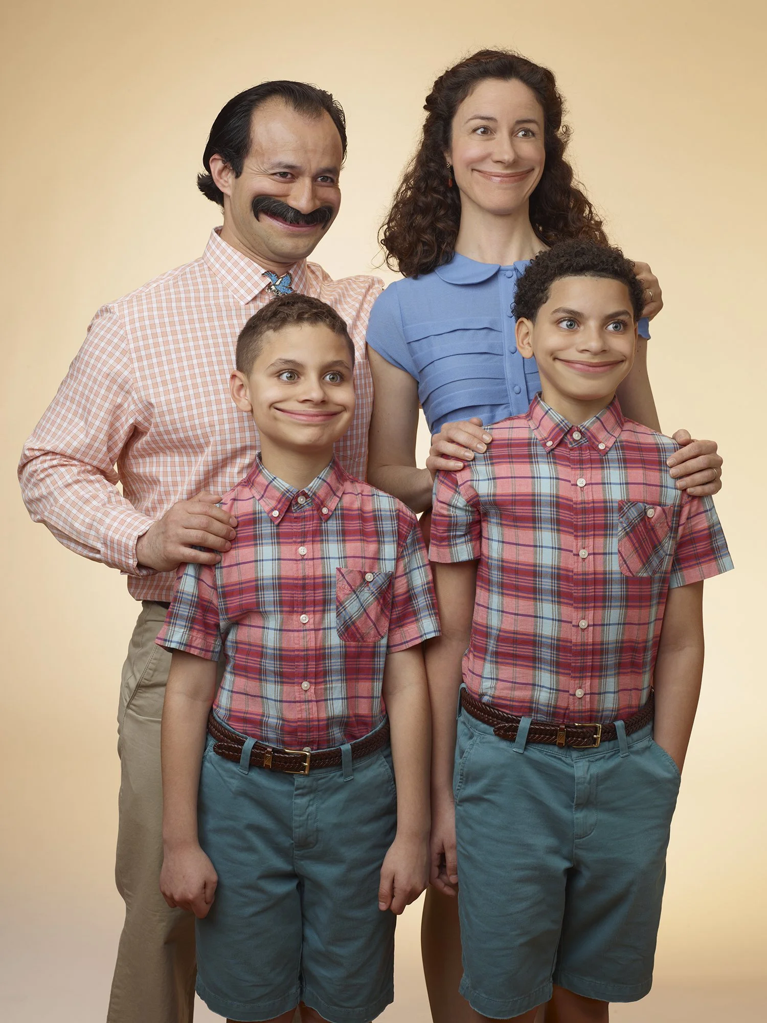 A family of five, including a man, woman, two boys, and a girl, posing together against a beige background. The family is smiling and wearing casual, colorful clothing.