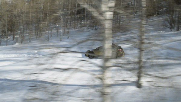 A black car driving through a snow-covered forested area with trees and snow on the ground.