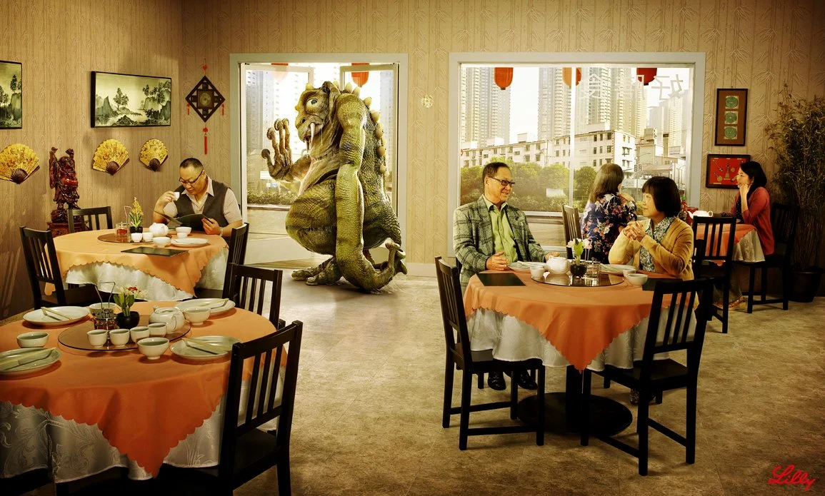 A restaurant with several tables set for dining. There are four people eating at different tables, and a large sculpture of a mythical creature resembling a dragon or lizard near the window. The restaurant has wooden walls decorated with fans, painti