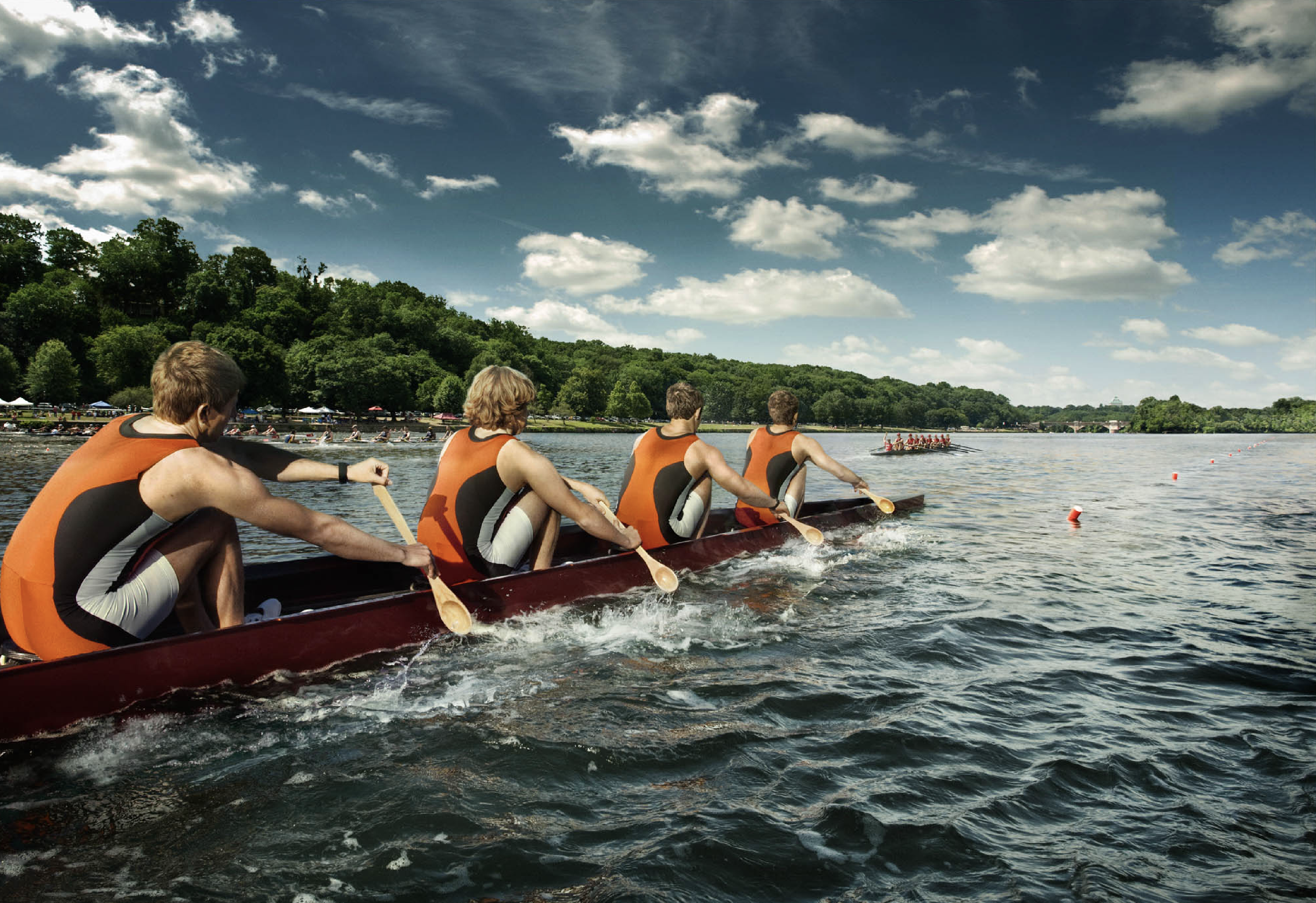 A team of rowers in a dragon boat on a lake, paddling in unison under a partly cloudy sky.