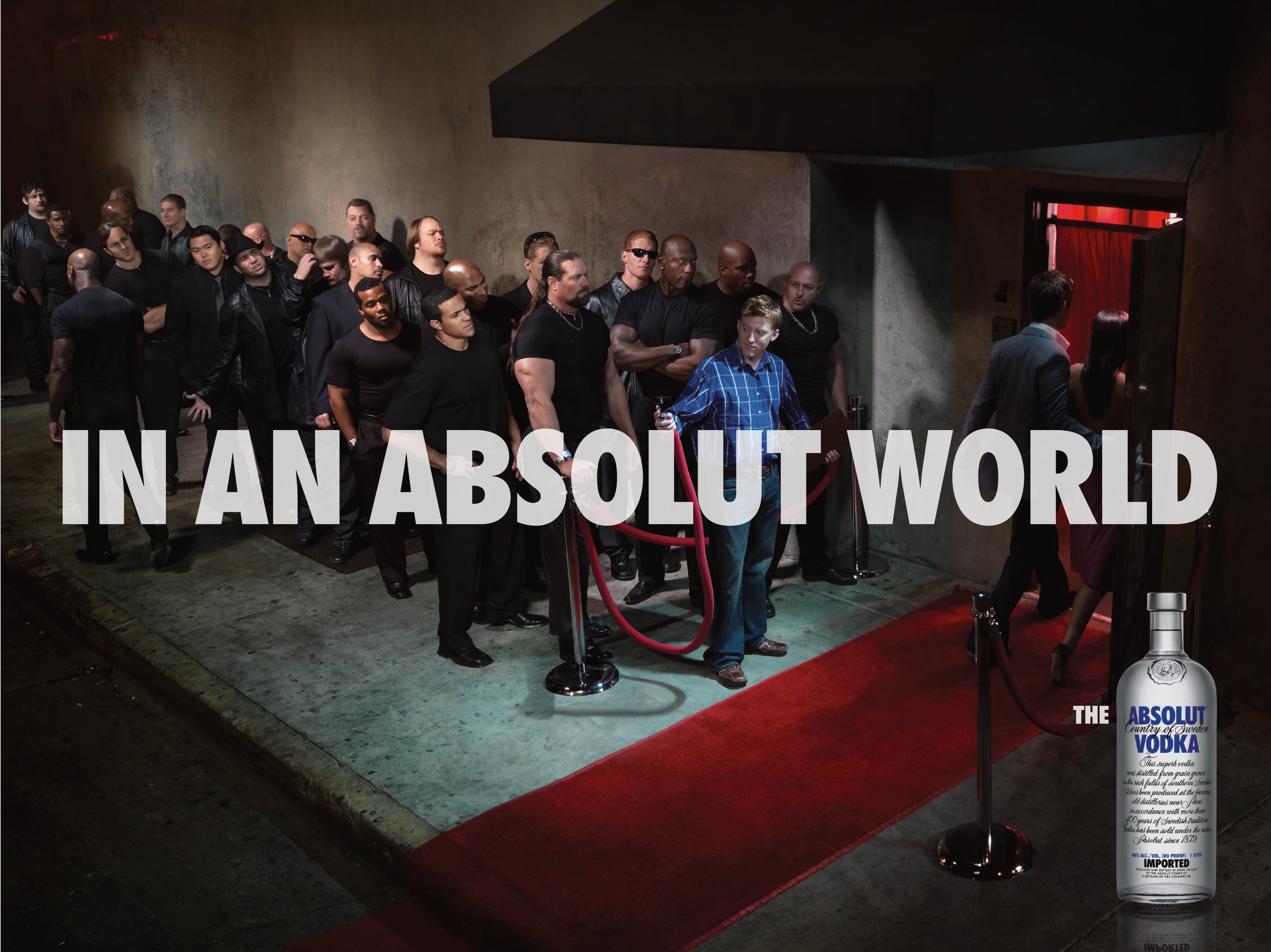 Line of diverse people waiting outside an entrance with a red carpet, some entering and some waiting in line, in an urban setting at night. There is a bottle of Absolut Vodka in the bottom right corner.