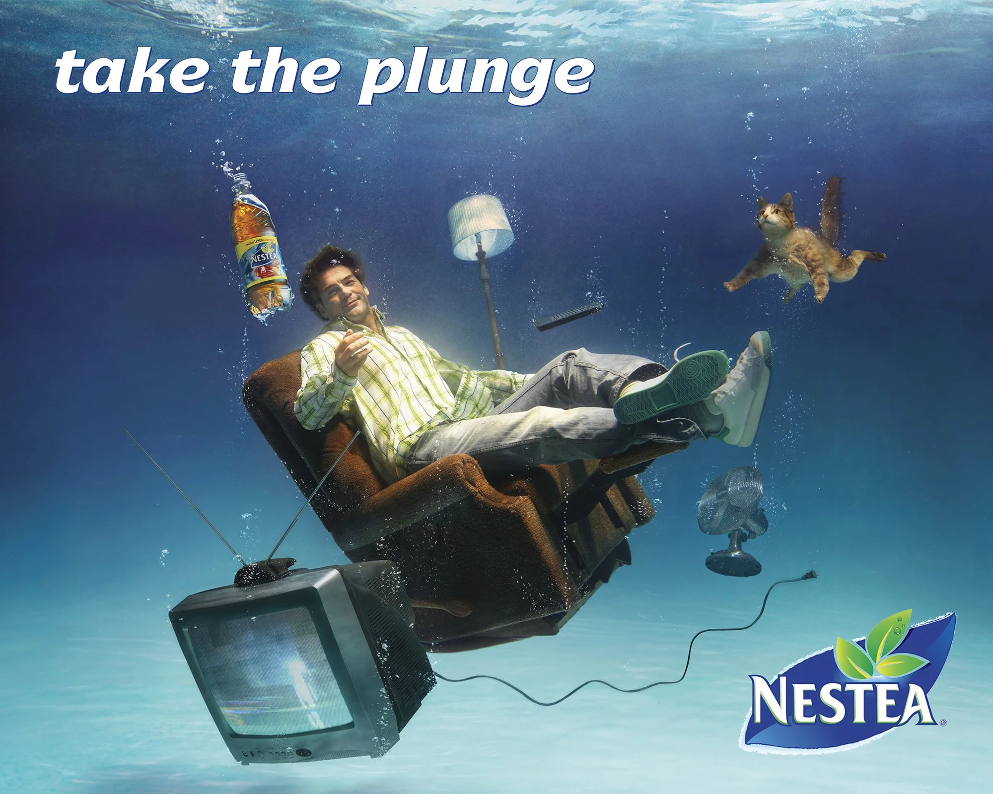 A man sitting on a recliner underwater with a beer in hand, surrounded by a vintage television, a cat, a lamp, a remote control, and a fan, with the text 'take the plunge' and the Nestea logo.