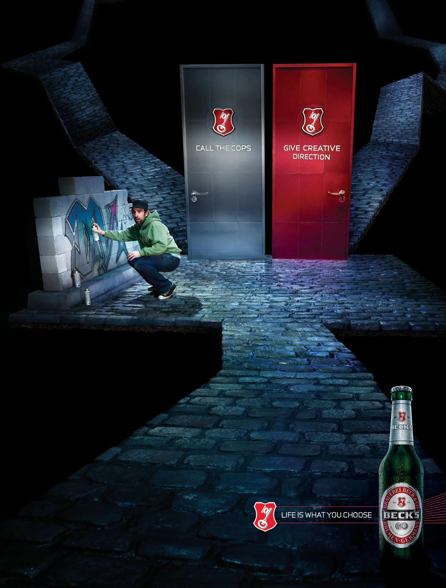 A man crouching on cobblestone street near graffiti wall, with two closed doors behind him labeled 'Call the Cops' and 'Give Creative Direction', and a large beer bottle in the foreground with a Beck's logo. The scene is dark and surreal.