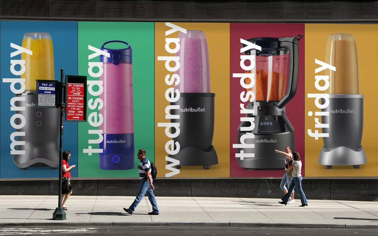 A large colorful outdoor advertisement displays various Nutribullet blenders and products with the slogans "monday," "tuesday," "wednesday," "thursday," and "friday." Pedestrians walk along the sidewalk in front of the advertisement.