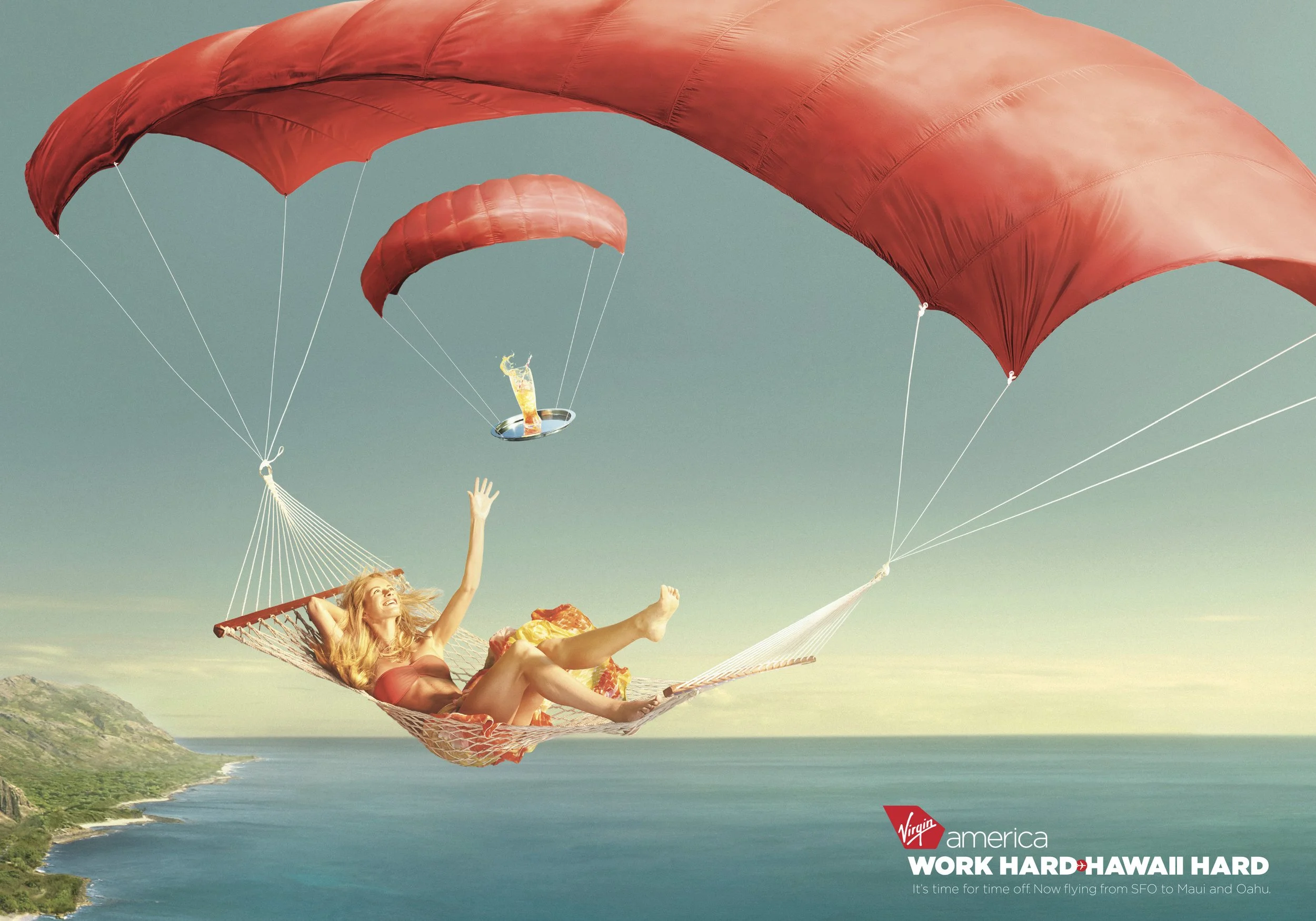 A woman relaxing in a hammock suspended from red parachutes flying over the ocean and coastline. The image has Virgin America branding and the text 'WORK HARD, HAWAII HARD'.
