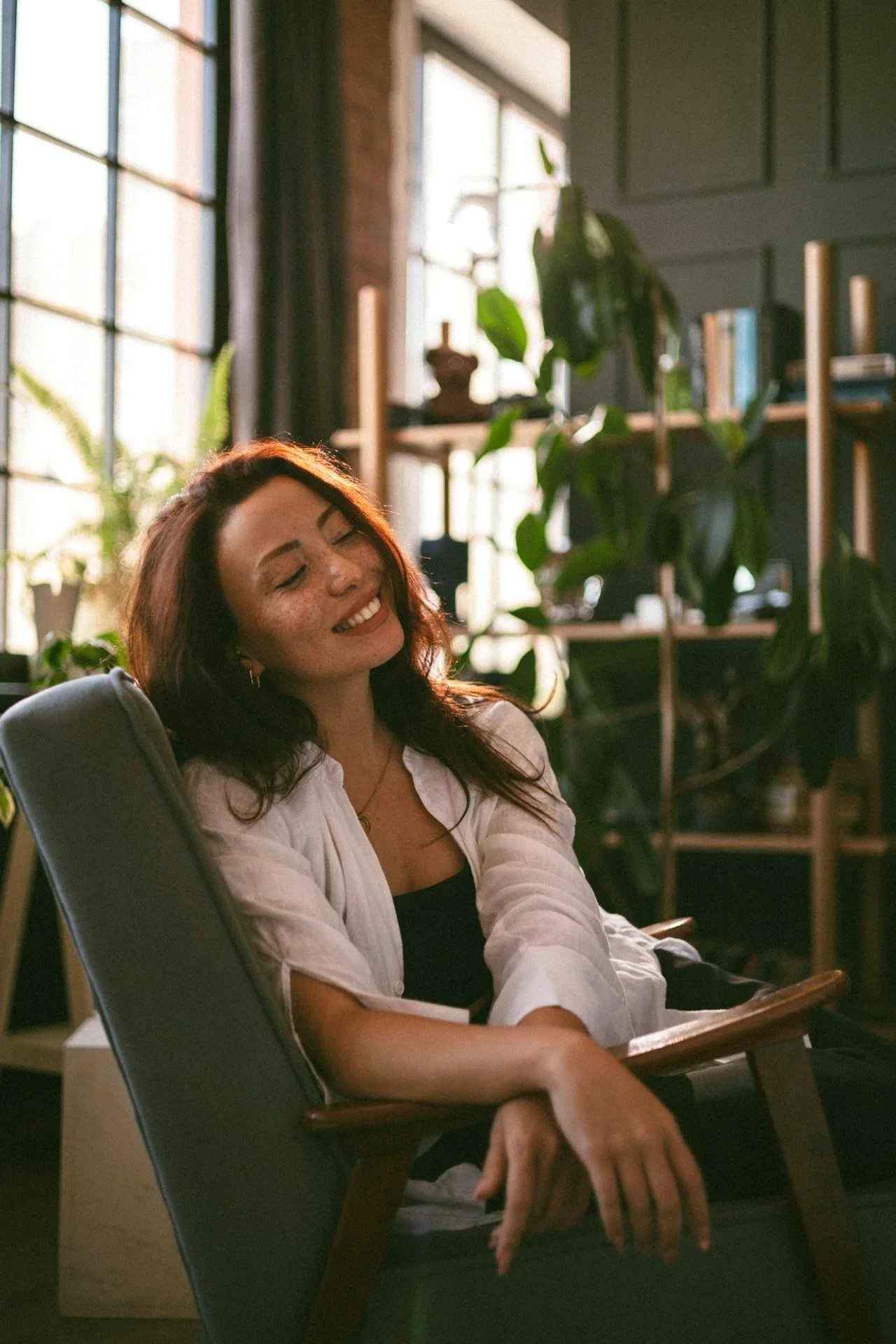 Person sitting comfortably, smiling to themselves in a room with plants.