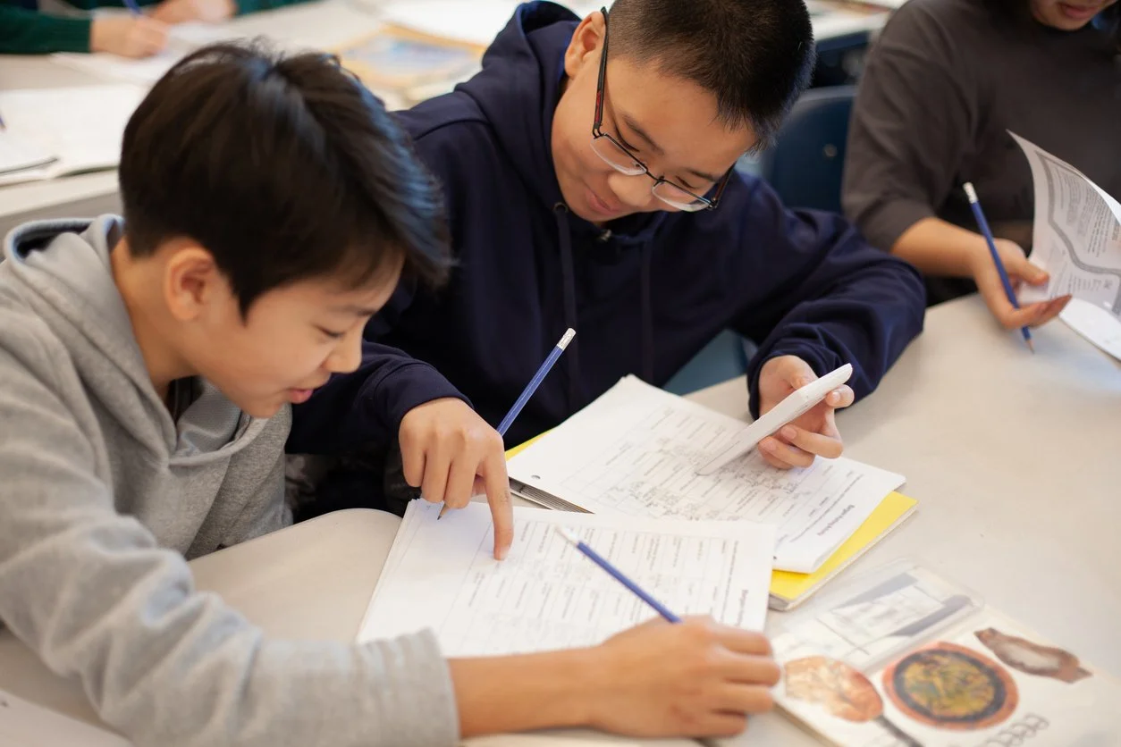 Two students are studying and taking notes at a table in a classroom.