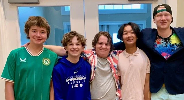 Group of five young people standing together indoors, smiling at the camera.