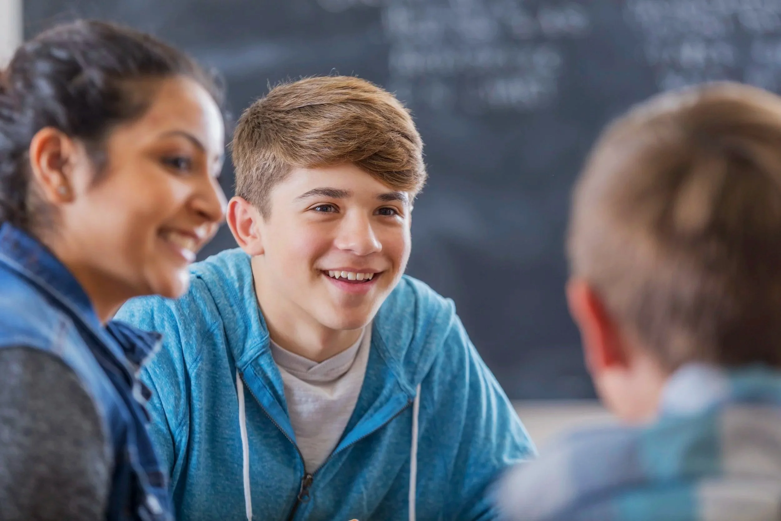 A group of three teenagers talking and smiling in a classroom.