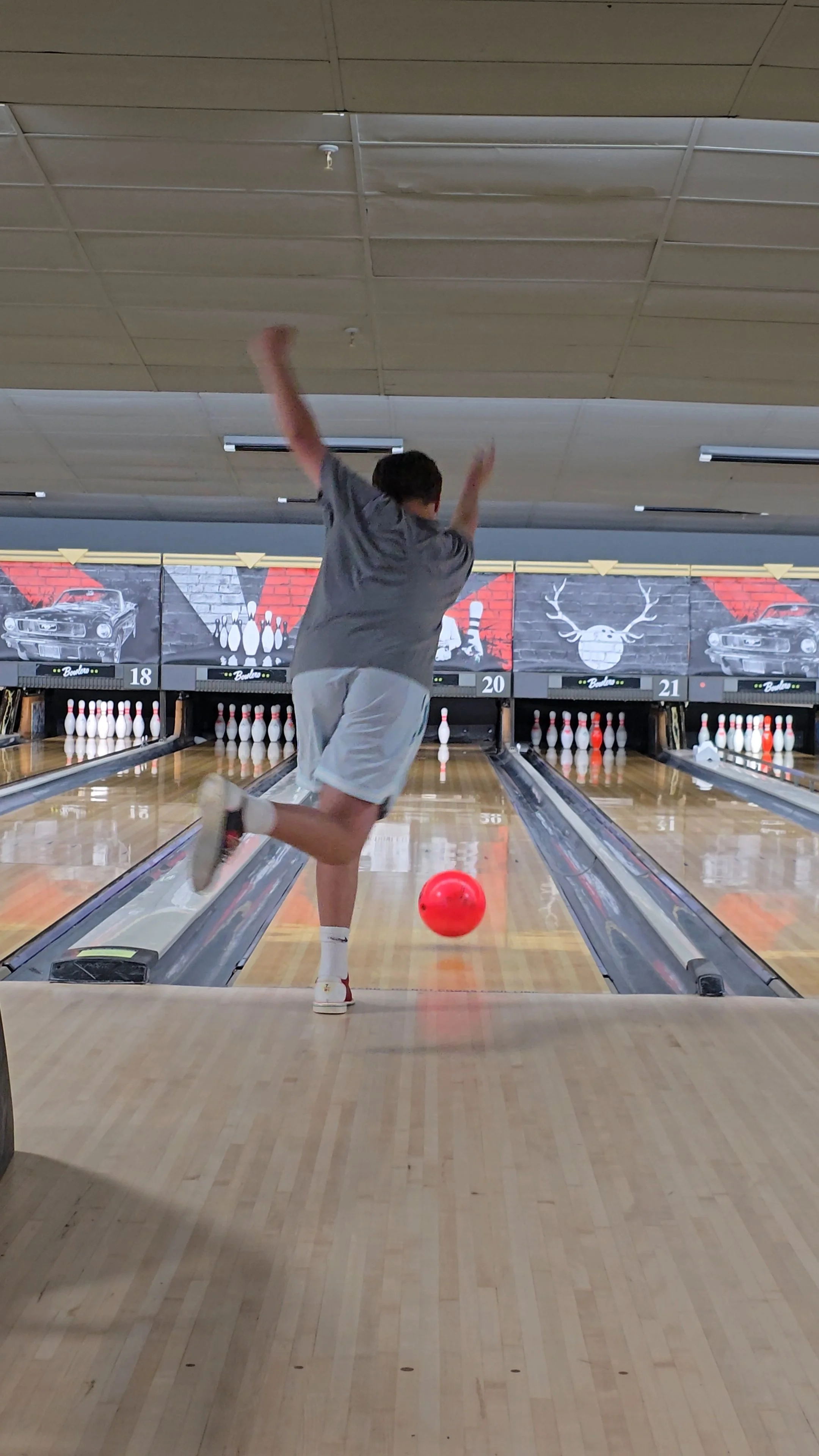 A person bowling at a bowling alley, releasing a red bowling ball down the lane.