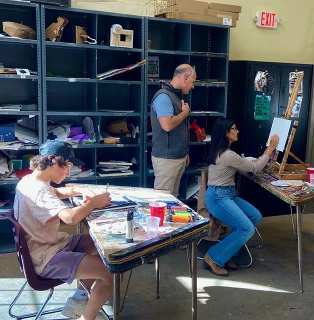 A boy drawing at a table with art supplies in front, a woman painting on a canvas at an easel, and a man observing in an art classroom or studio with shelves filled with art materials in the background.