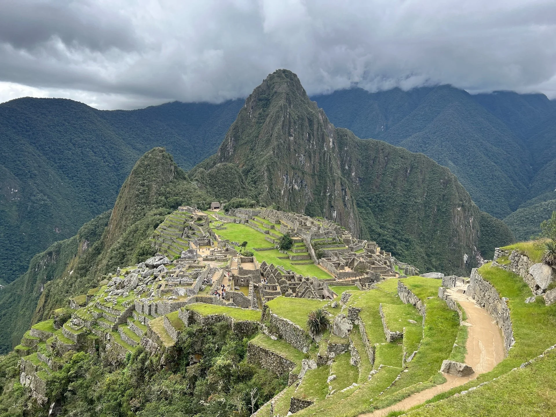 Ancient Incan ruins at Machu Picchu with terraced fields, stone structures, and lush green mountains under cloudy sky.