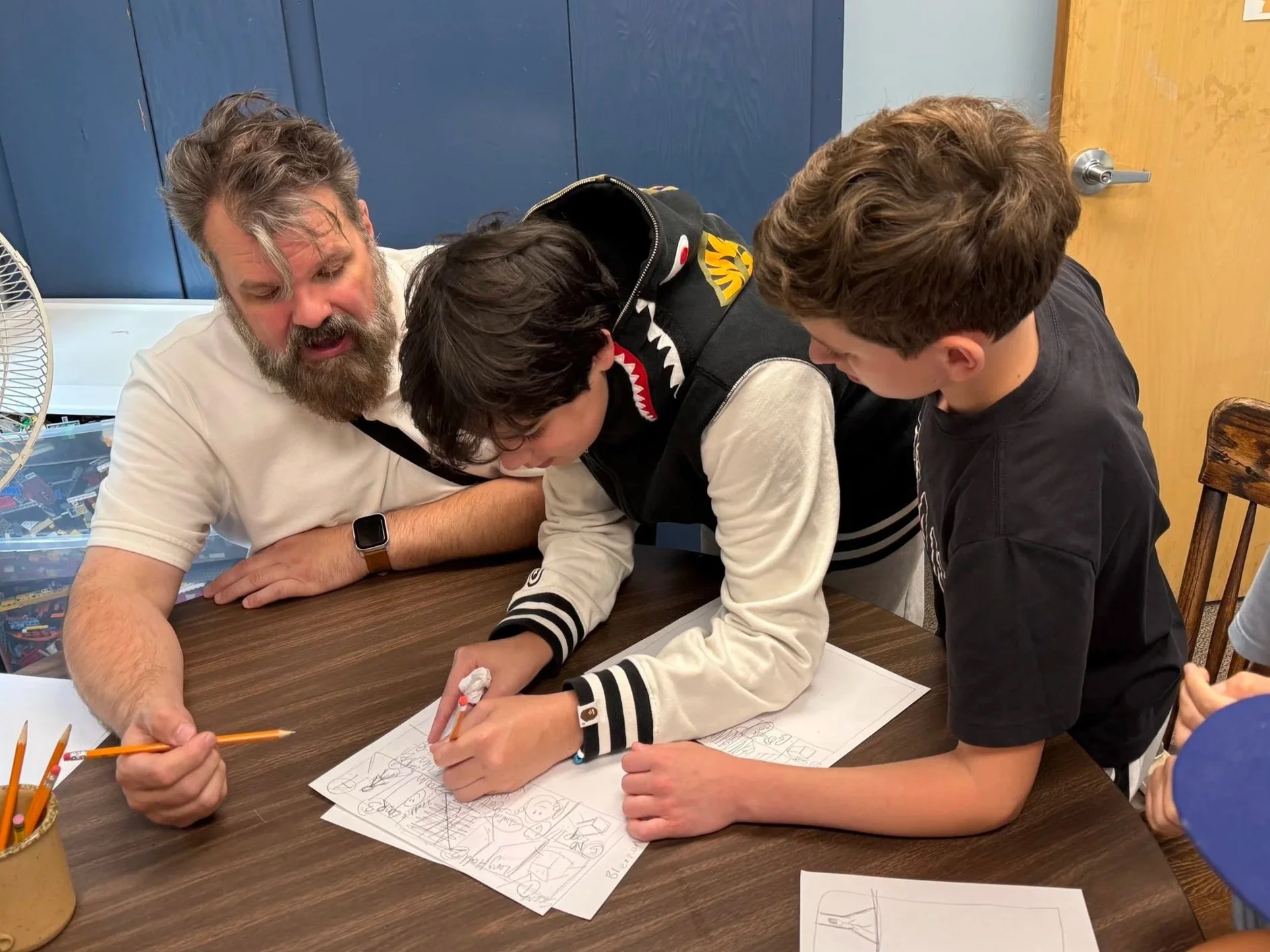 A man with a beard and two boys working together on a drawing at a table.