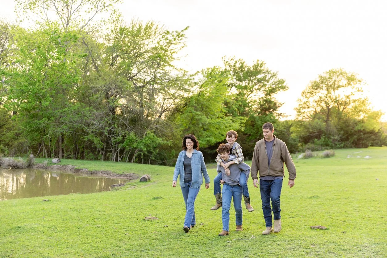 Group of four people walking on grass near a pond with trees in the background during sunset.