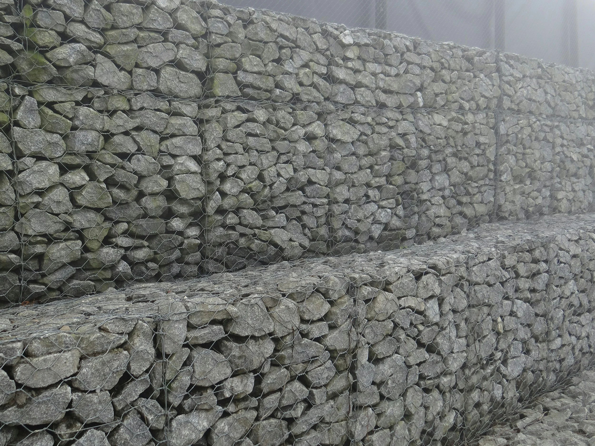 Stacked rocks enclosed in wire mesh, forming a gabion wall.