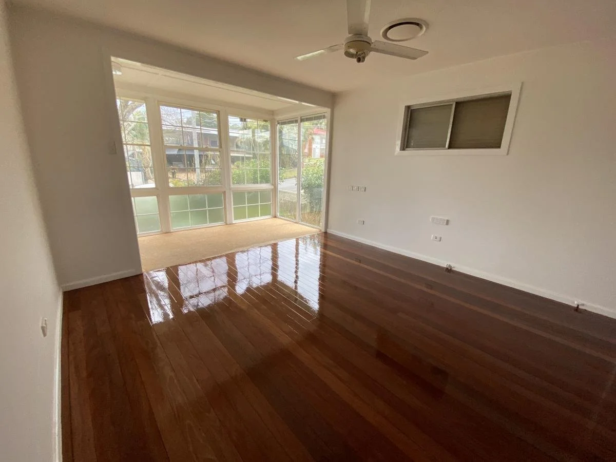 Empty room with polished wooden floor, white walls, ceiling fan, large window with glass tiles, and a small window on the adjacent wall.