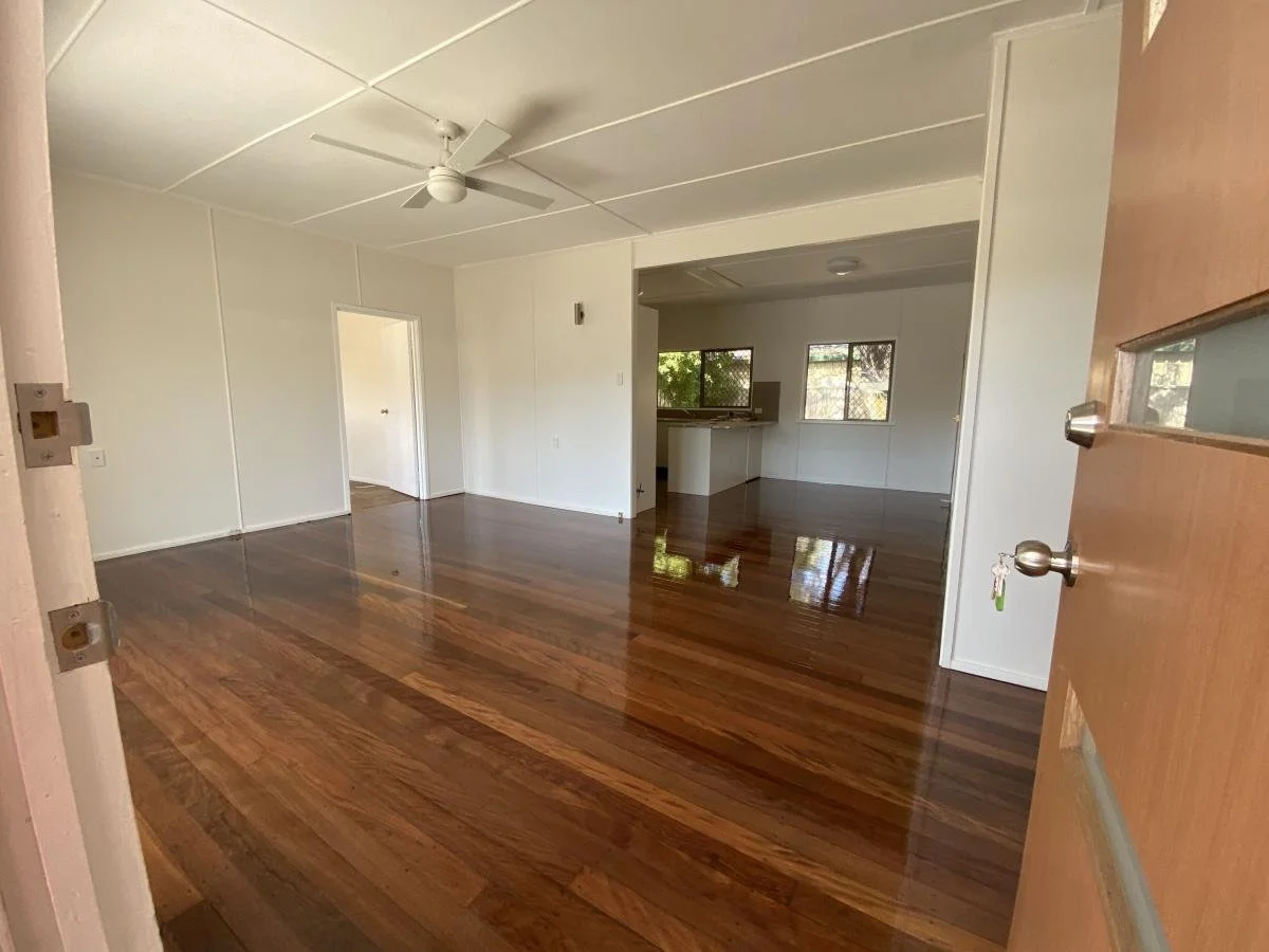 Empty room with polished hardwood floors, white walls, a ceiling fan, and a doorway leading to another room. An open door is visible on the right.