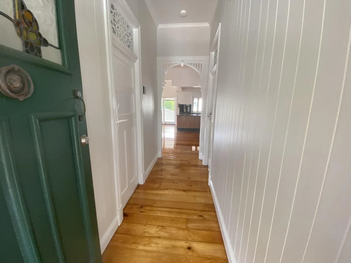 Hallway with wood floors, white walls, arched entry to a room with deck and a kitchen in the background.