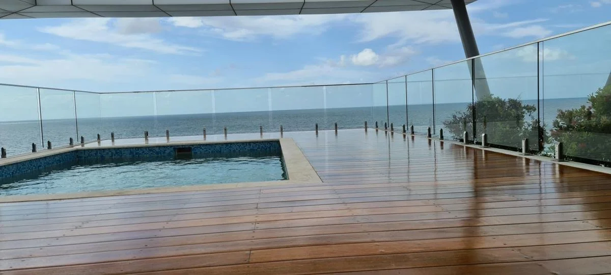 Ocean view from a rooftop deck with a small hot tub, wooden flooring, and glass railing.