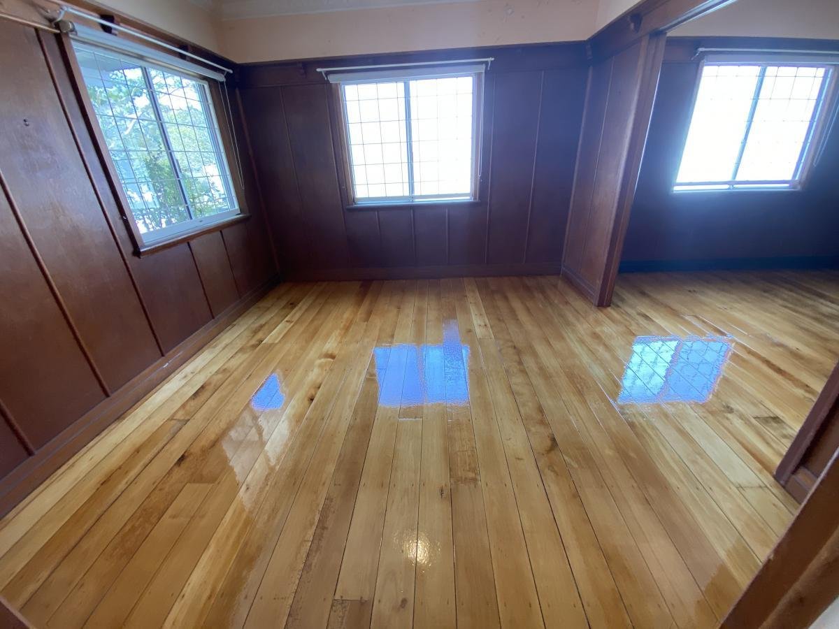 Empty room with shiny hardwood floor and three windows with grid-patterned glass, dark wooden wall paneling, and beige ceiling.