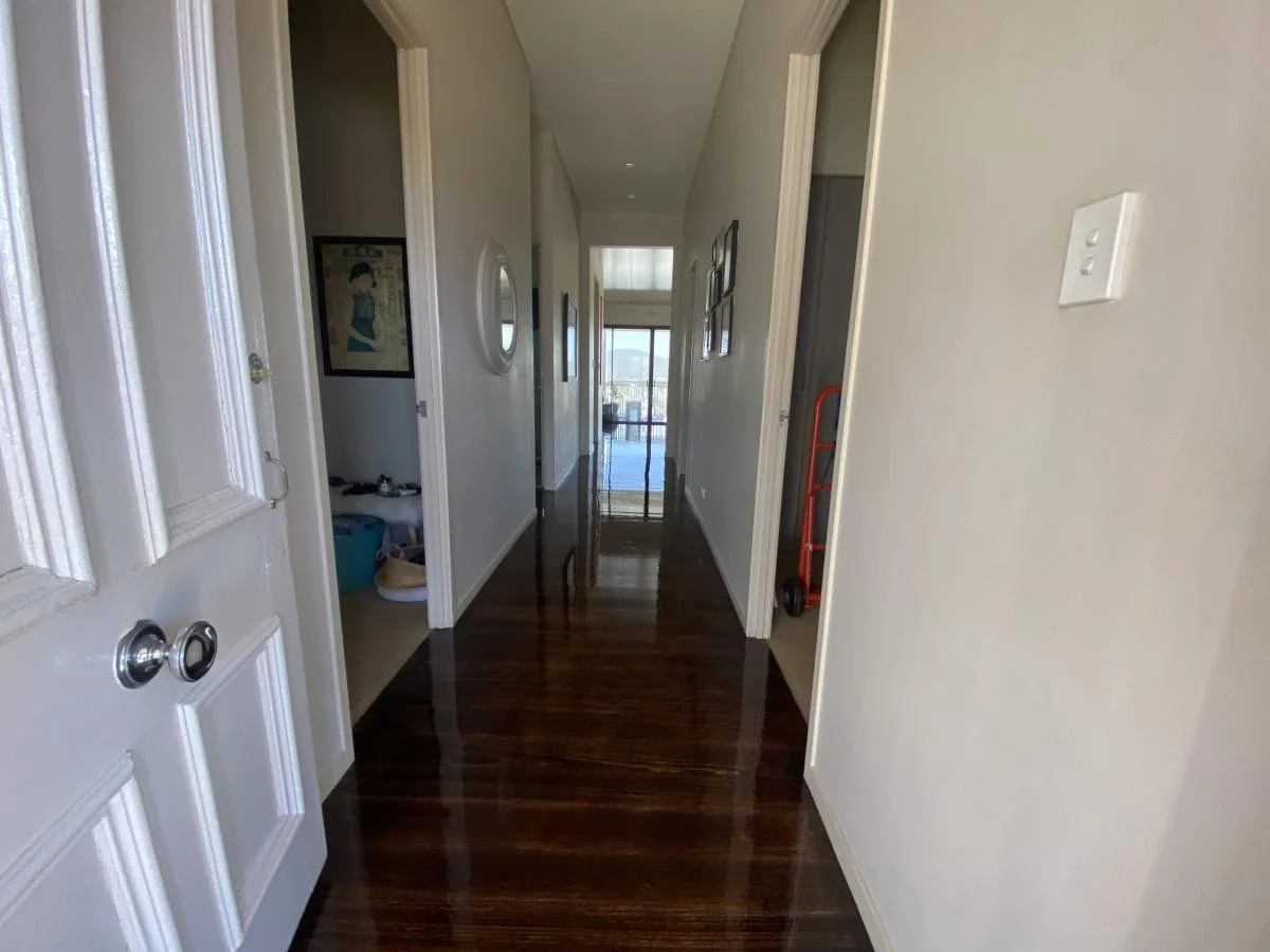 Hallway with polished wooden floors and artwork on the walls, leading to a balcony with glass doors outside.