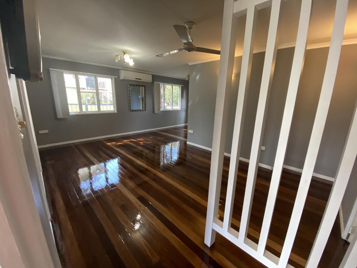Empty living room with hardwood floors, gray walls, two windows, a ceiling fan, and an air conditioning unit.