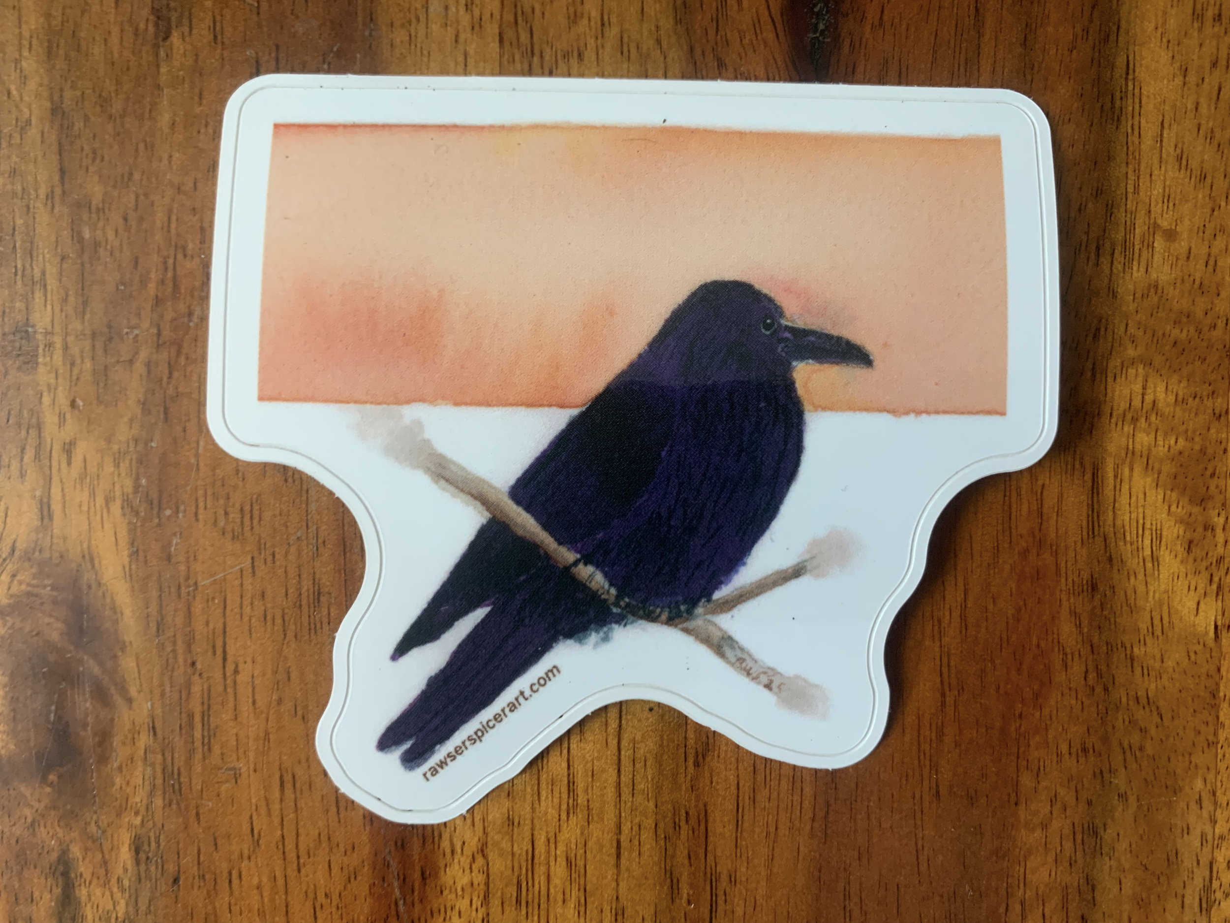 Image of sticker picturing a common raven with a horizontal orange stripe in the background