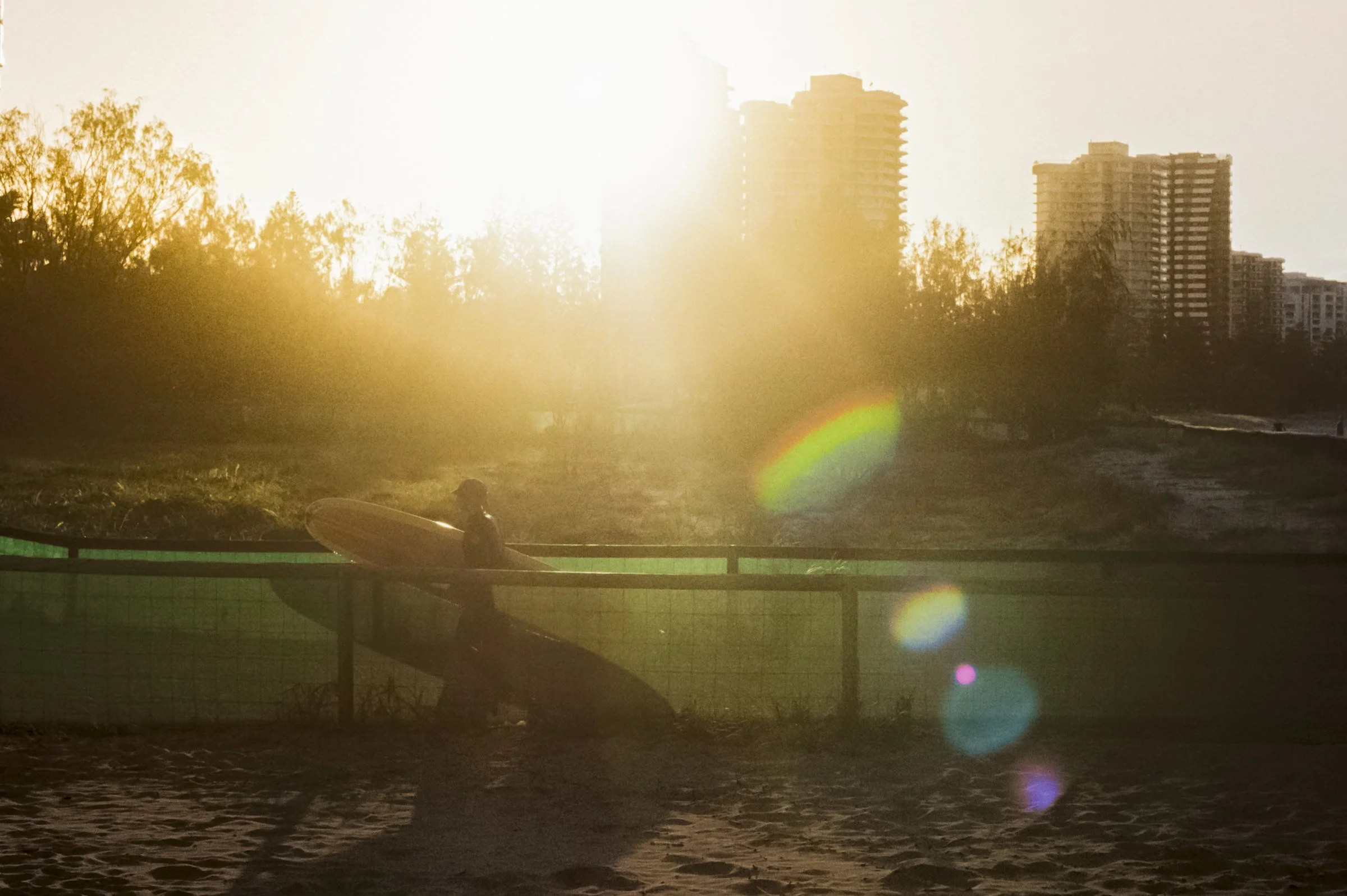 A surfer walking at sunset back to their car with lots of lens flare shot on film