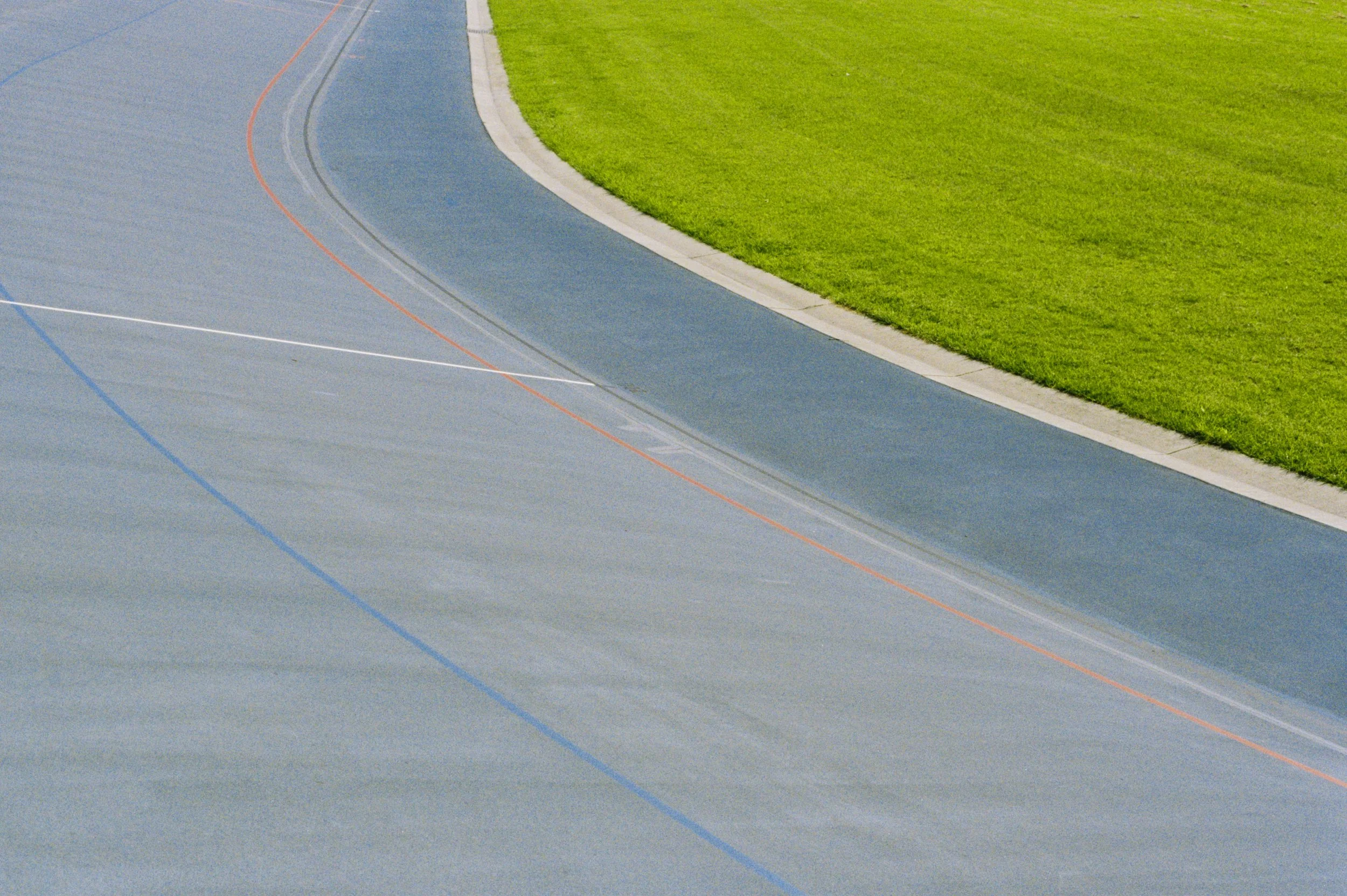 An outdoor running track with multicolored lines, surrounded by a grassy field.