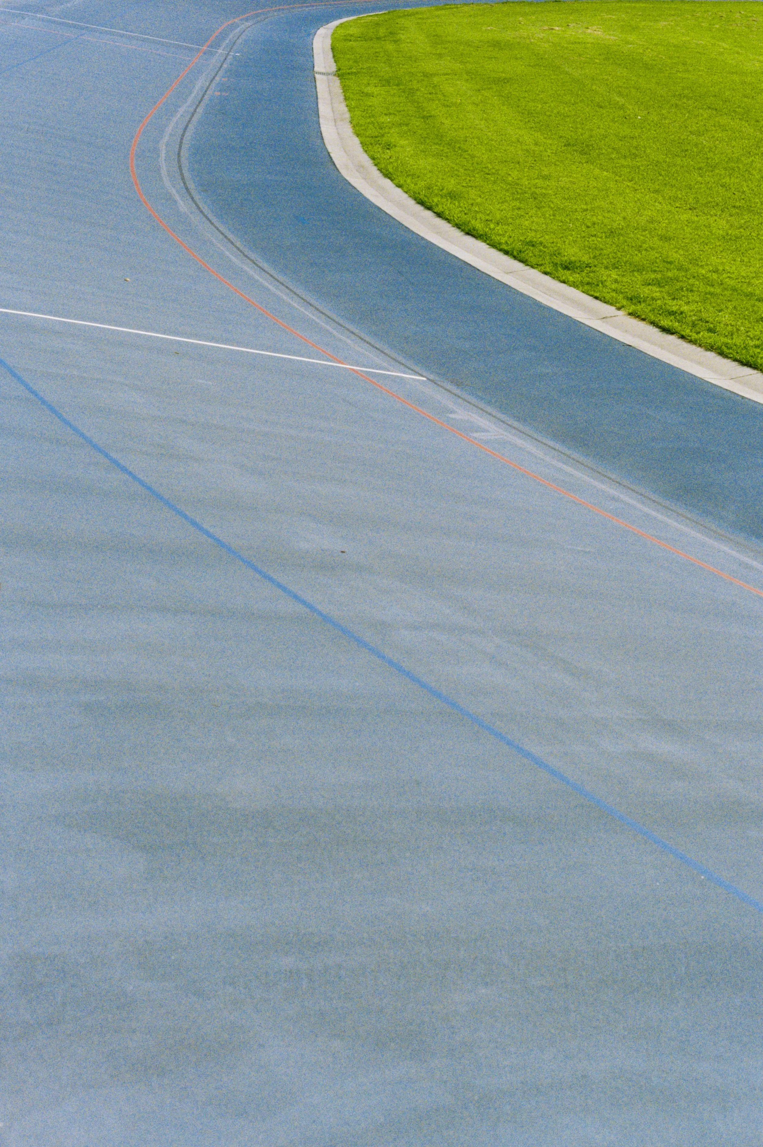 Close-up of an outdoor running track with a grassy field next to it, showing the curved edge of the track and grass.