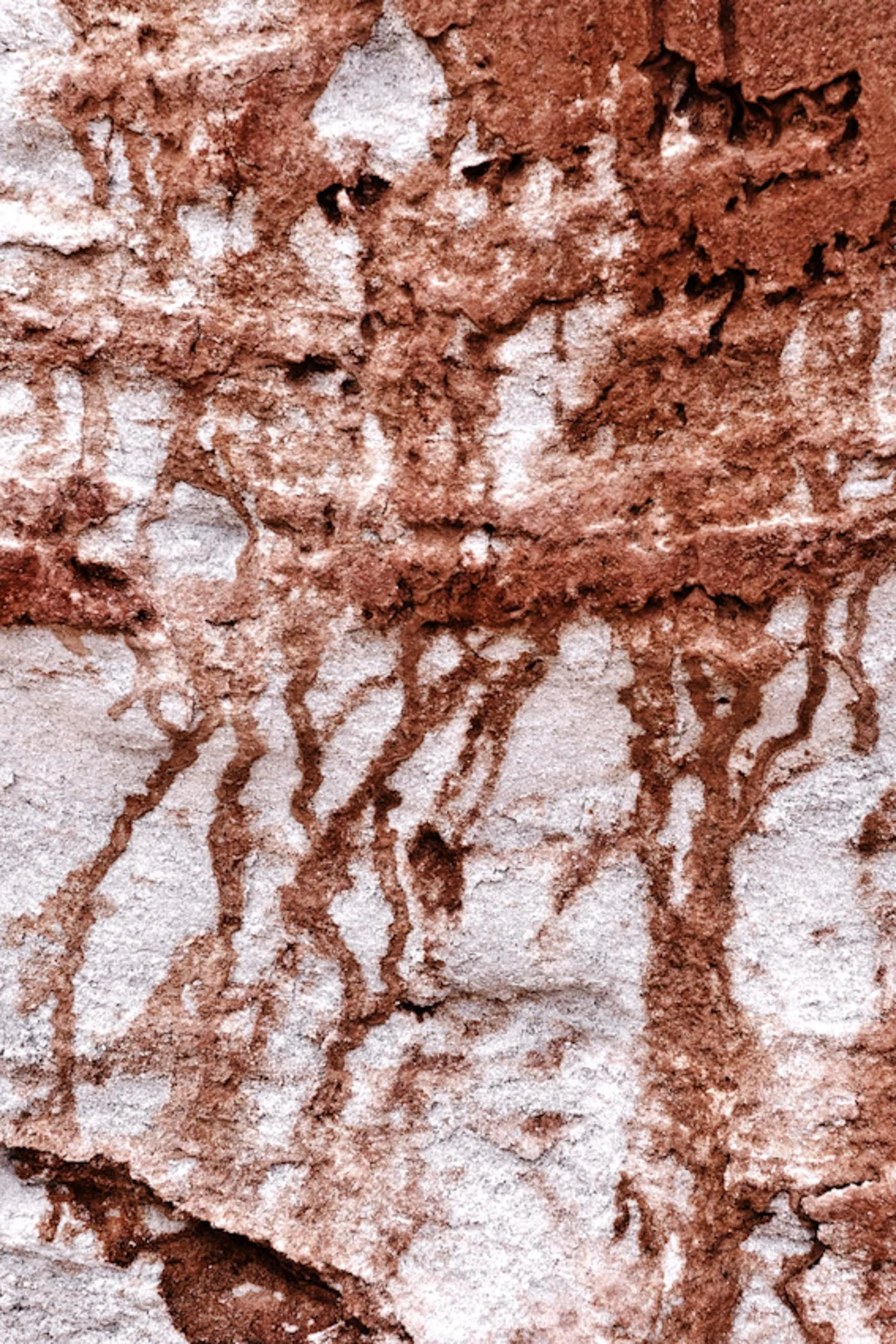 Close-up of an old, weathered brick wall with reddish-brown and white stones, showing cracks and uneven surface textures.