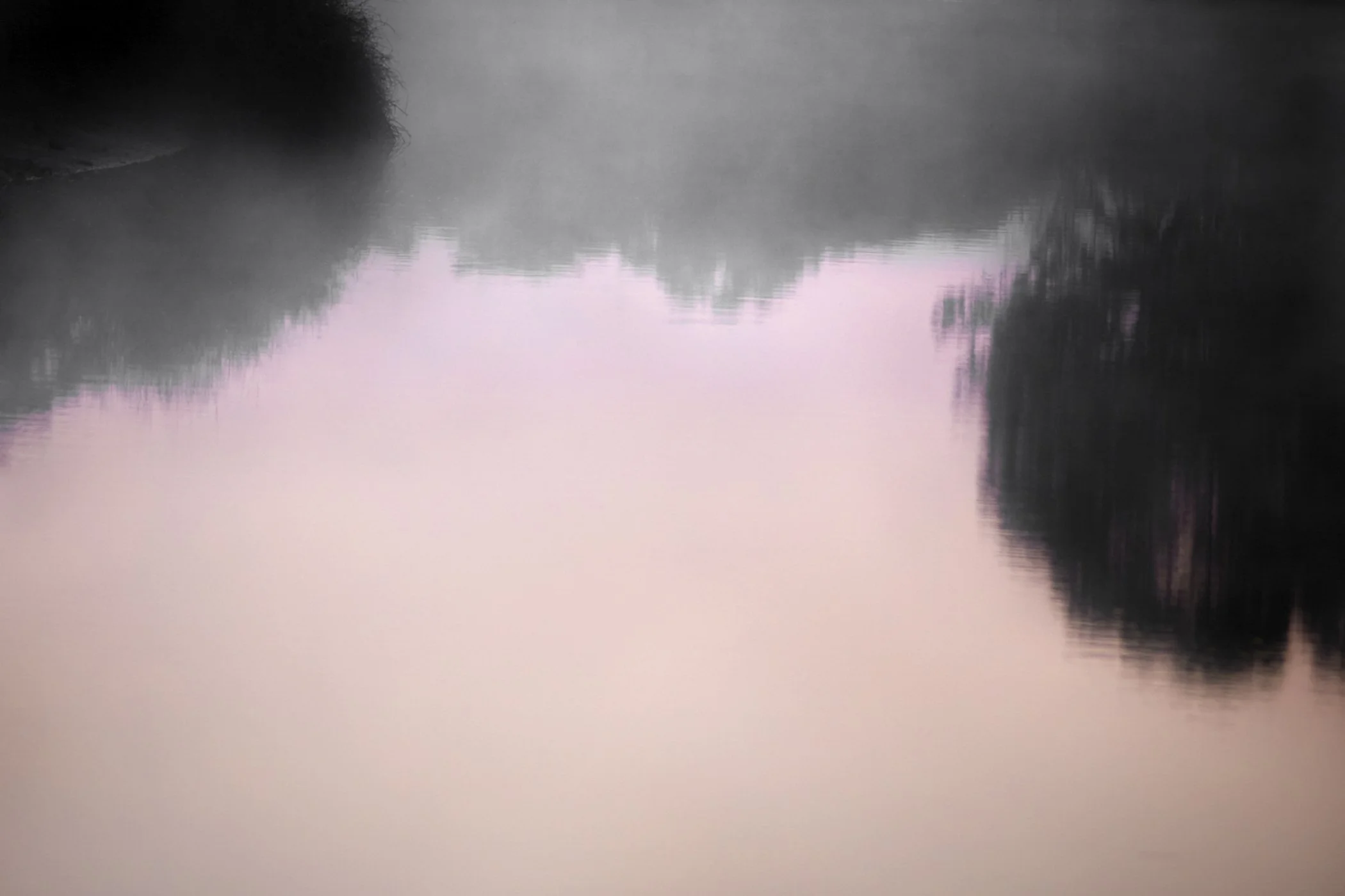 A foggy river scene at dawn or dusk with still water reflecting the silhouettes of trees on both sides.
