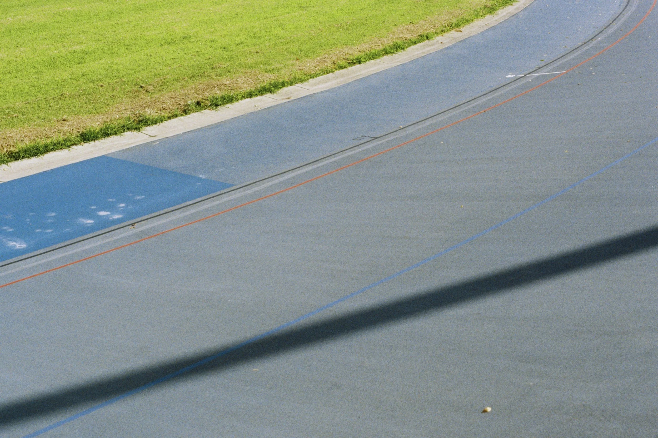An outdoor running track with a blue lane, marked with orange and blue lines, adjacent to a grassy field.