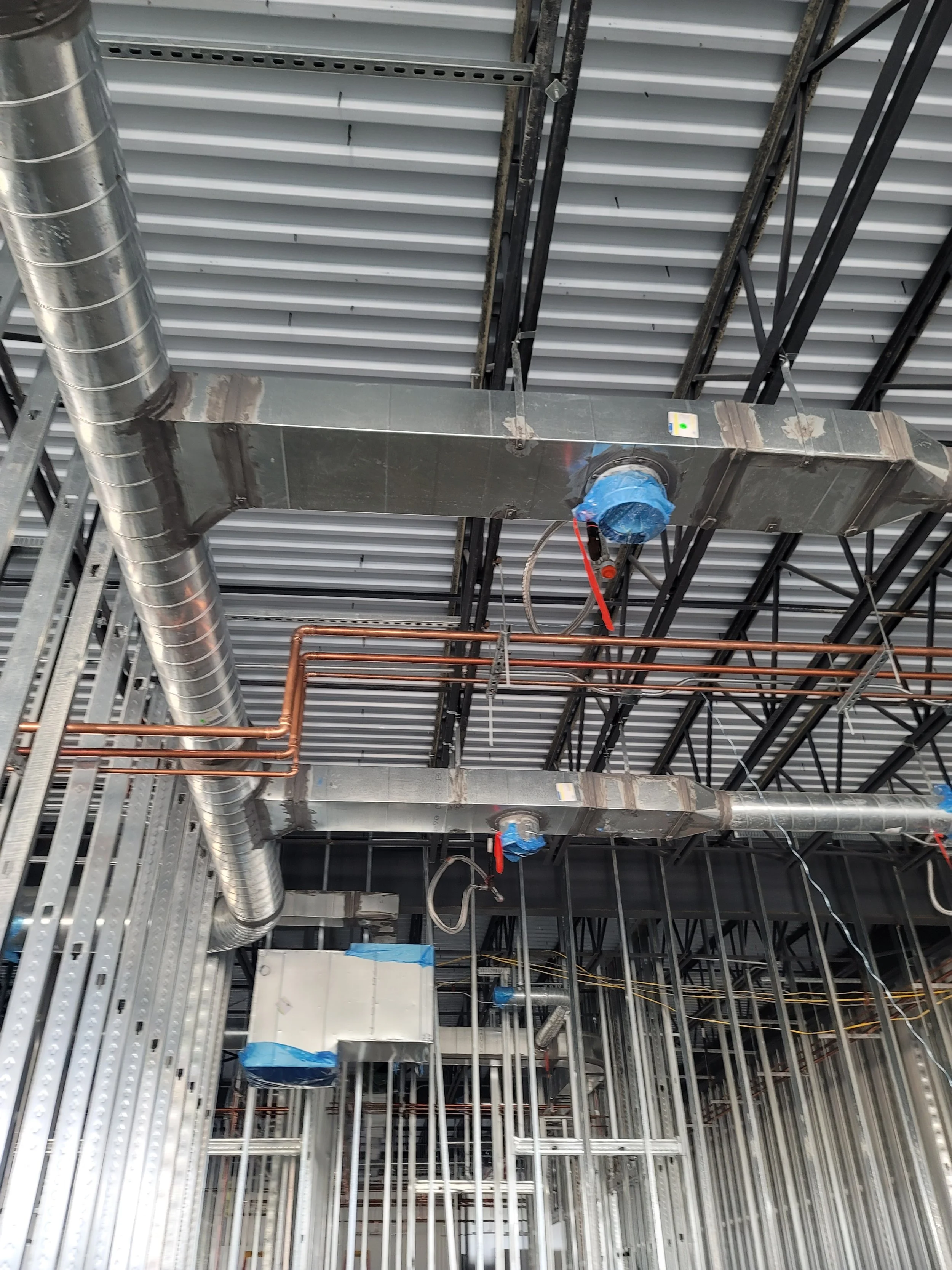 Ceiling construction with metal ducts, pipes, and wiring in a building under construction.