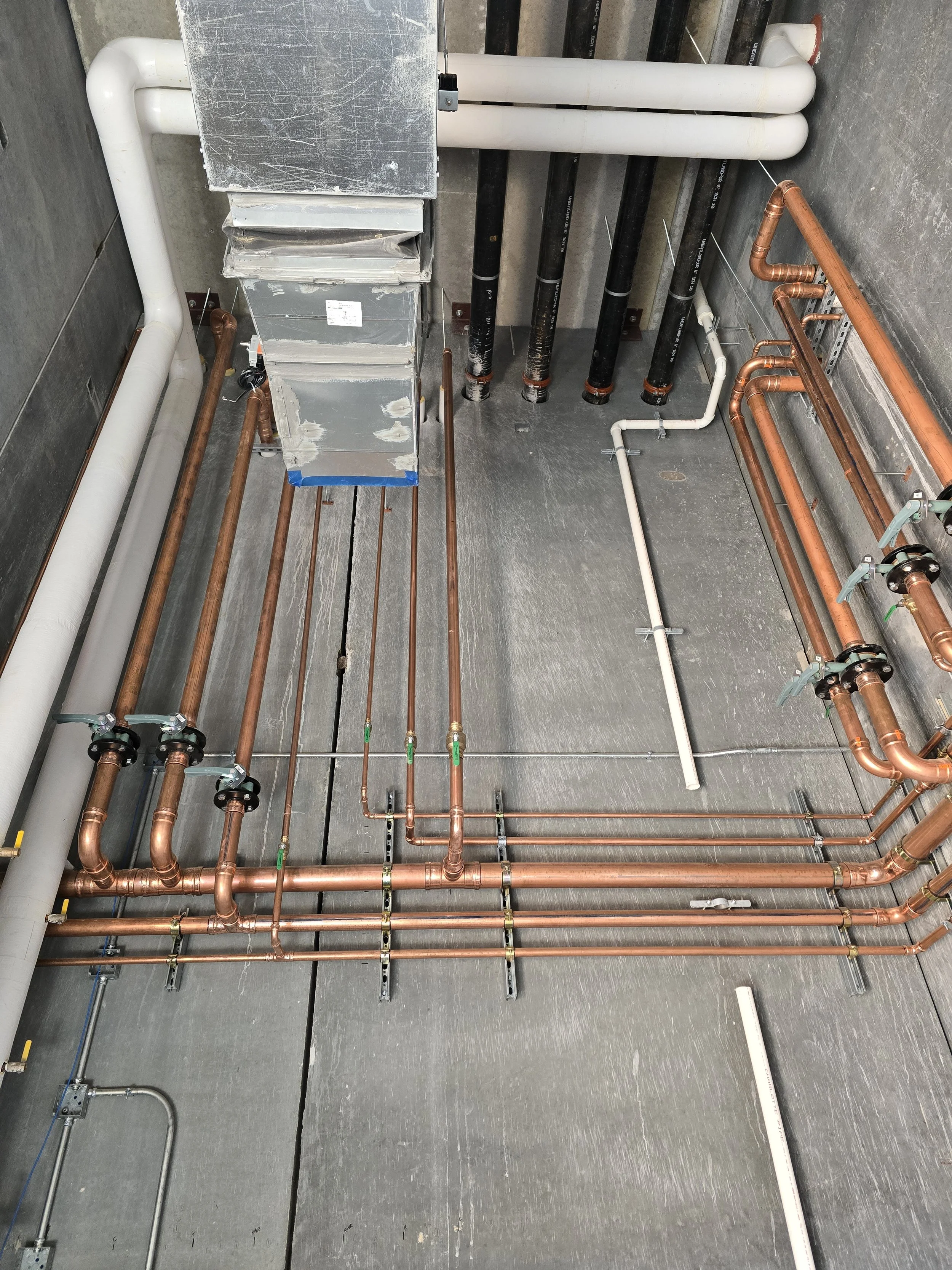 Interior view of plumbing and HVAC system with copper pipes, PVC pipes, and metal ductwork in a utility room or ceiling space.