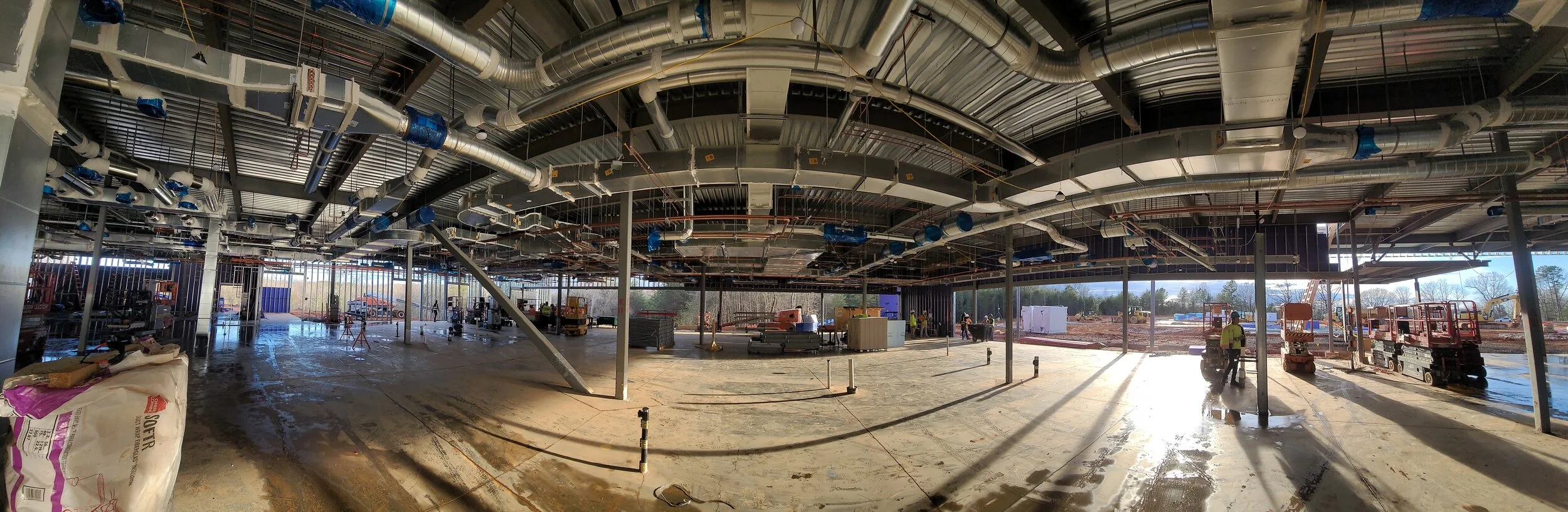 Construction site of a large building with exposed ductwork and construction workers working inside.