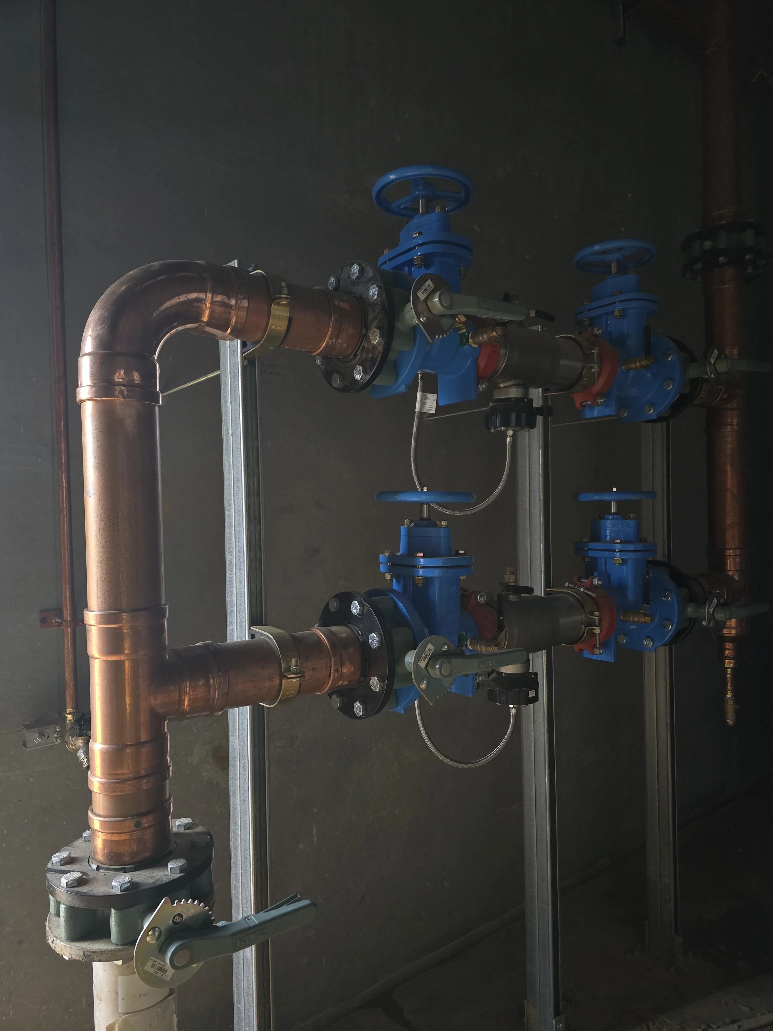 A plumbing system with copper pipes, blue valves, and black fittings mounted on a metal frame.
