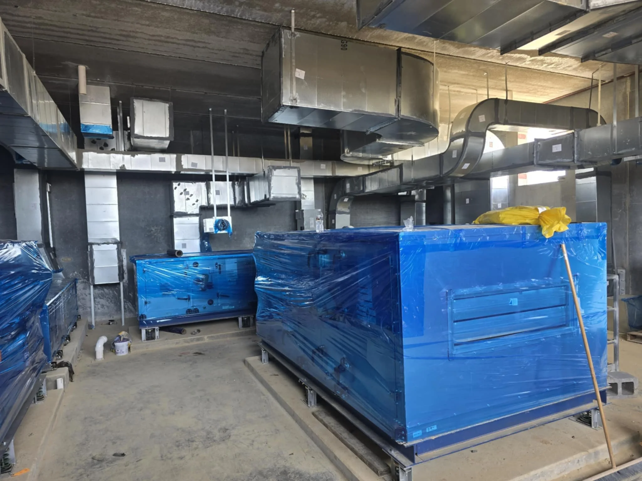 Construction site with large industrial HVAC ducts and machinery covered in blue plastic.