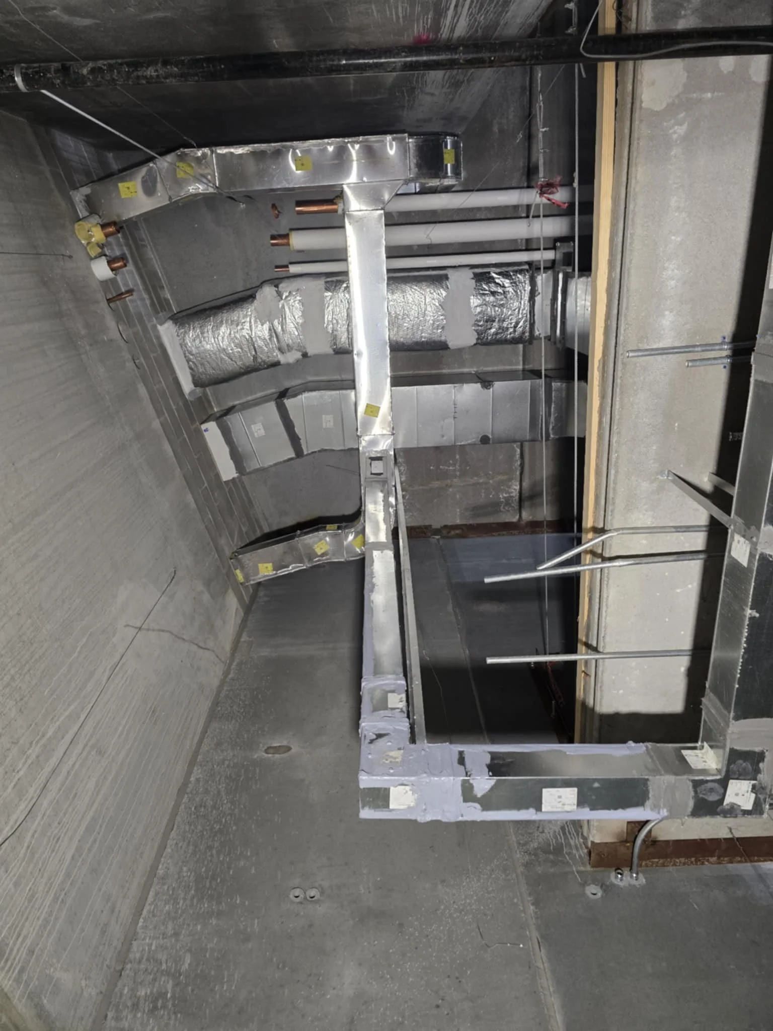 Construction site with exposed metal ductwork, pipes, and framing in a building interior under construction.