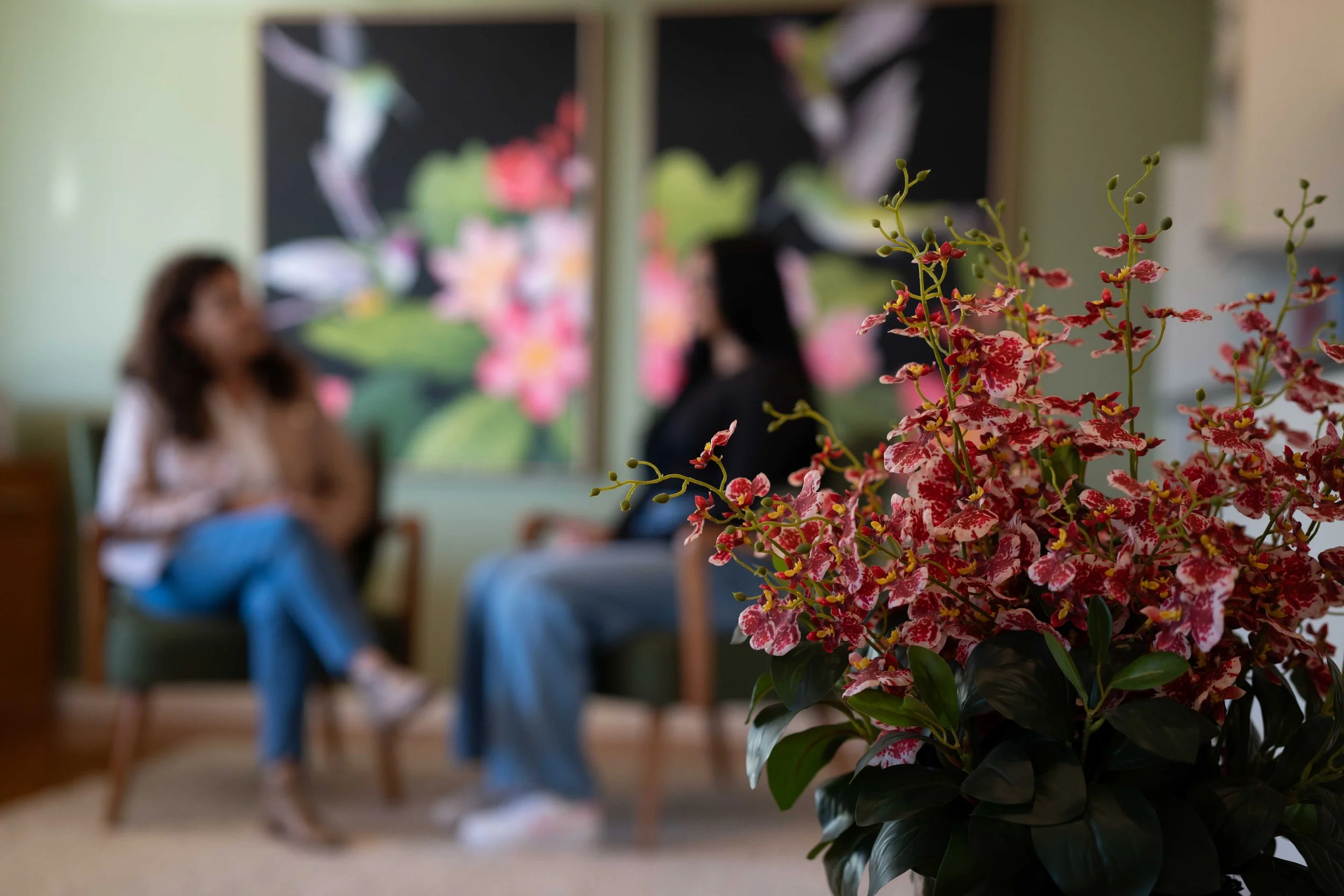Sue Dalby, Senior Counselling Psychologist, and young female blurred in background, vibrant pink and white flower arrangement in the foreground.