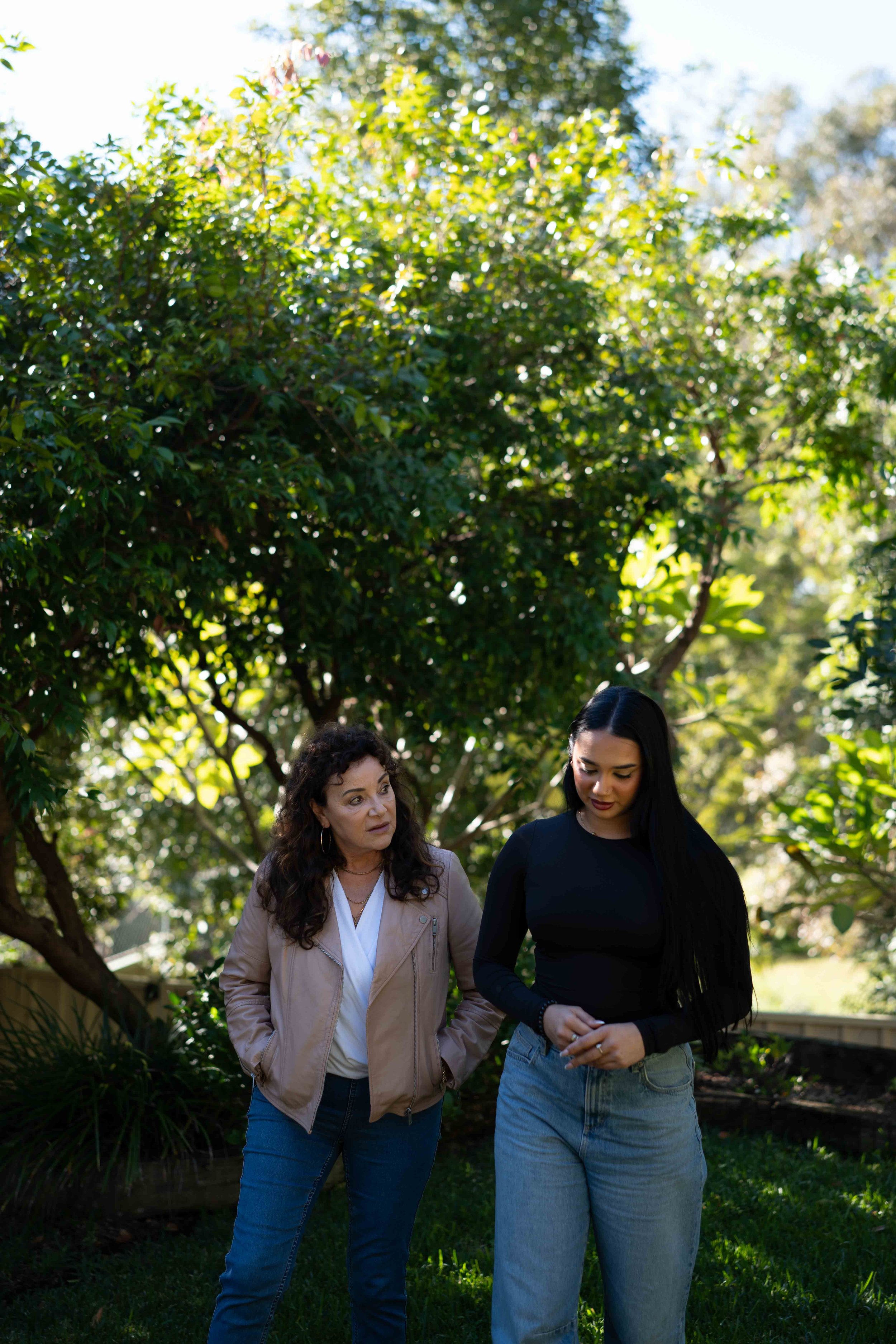Sue Dalby, Senior Counselling Psychologist, and a young female walking and talking in her garden with sunlight filtering through green trees.